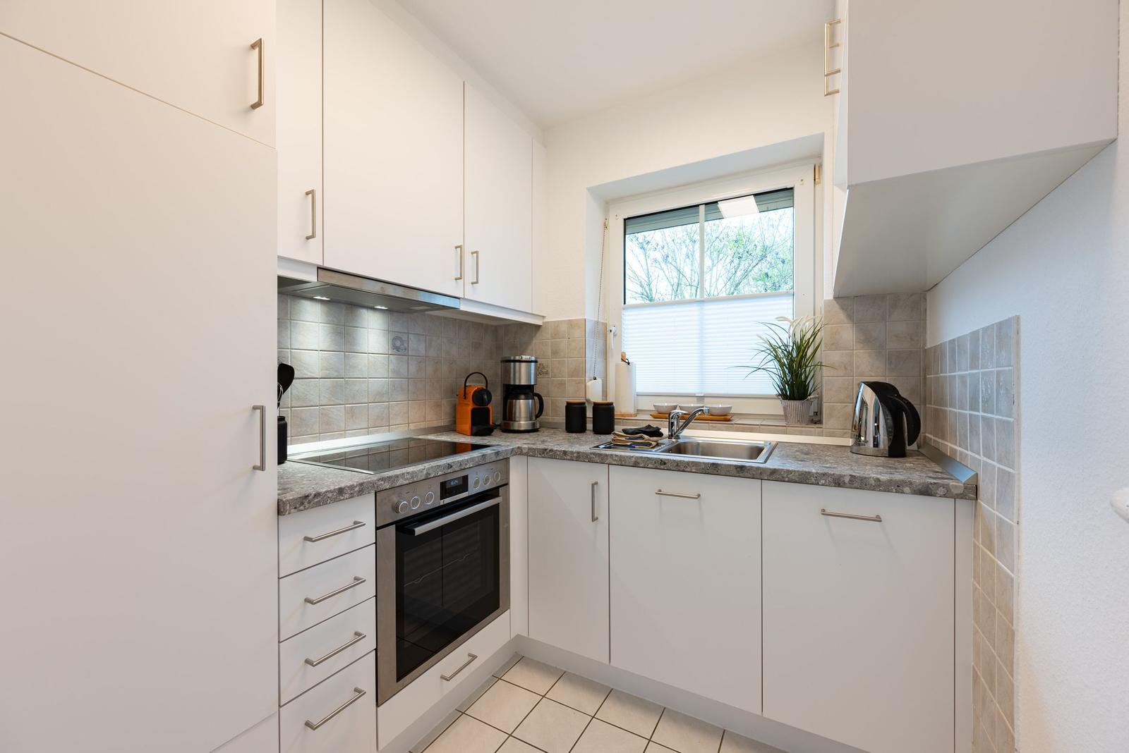 Moderne Küche mit weißen Schränken, Edelstahlgeräten und Fenster mit Blick nach draußen.