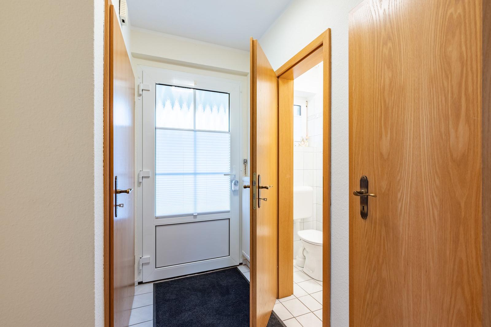 Hinter dem Eingang befindet sich ein Badezimmer mit Toilette und Fenster mit Jalousie.