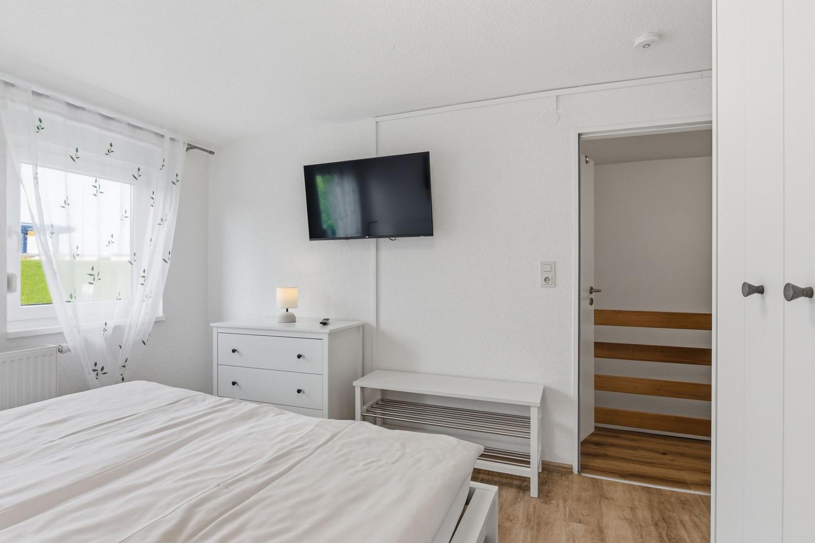 Schlafzimmer mit Bett, Schrank, Fernseher und Fenster mit Vorhängen.