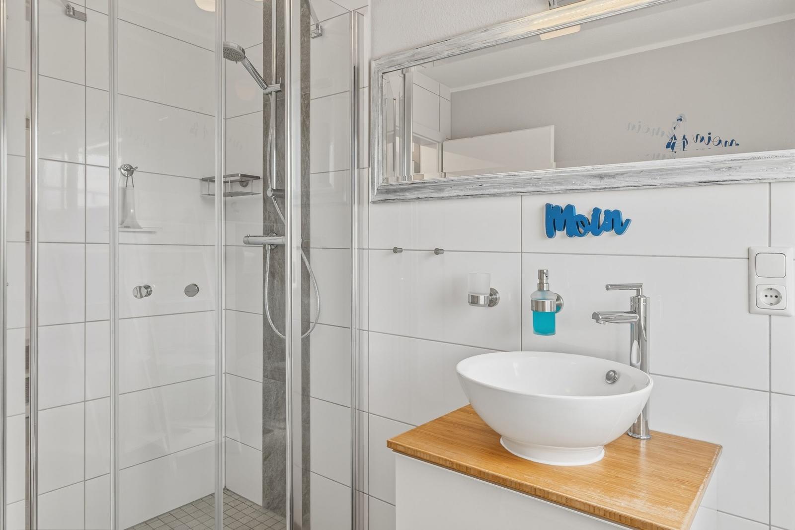 Badezimmer mit Dusche, Waschbecken und Spiegel. Wanddekoration mit Moin.