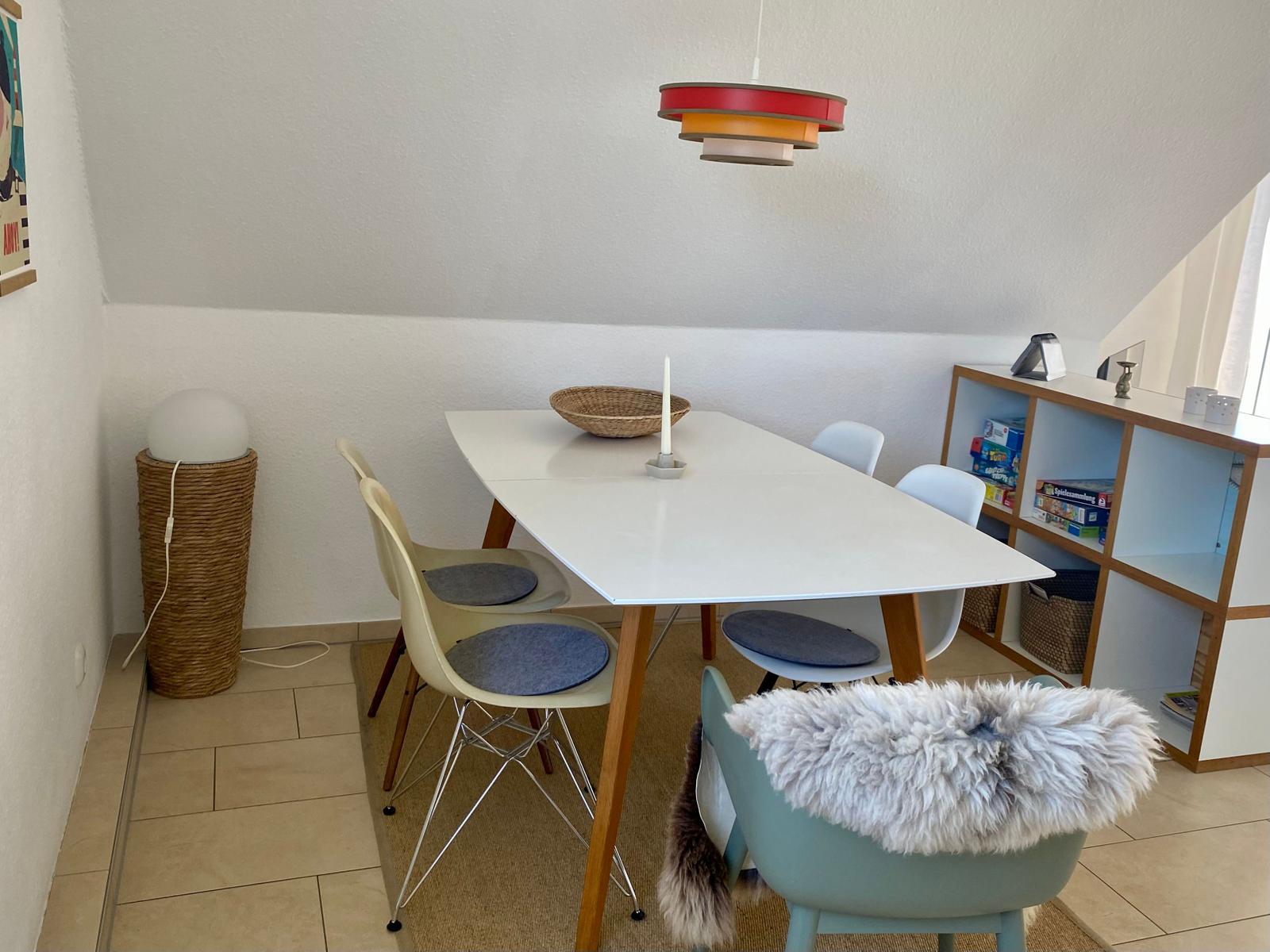 Essbereich mit weißem Tisch, Stühlen und einer bunten Decke.