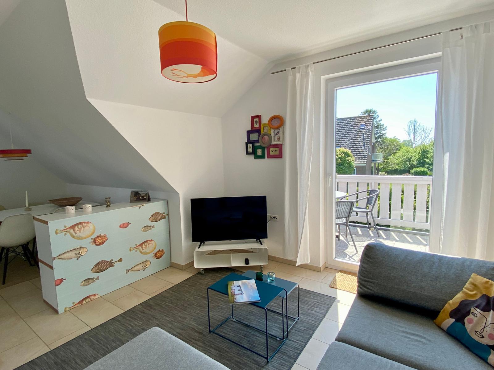 Wohnzimmer mit Sofa, TV und Balkonzugang. Decke geneigt, Wand mit Bilderrahmen.