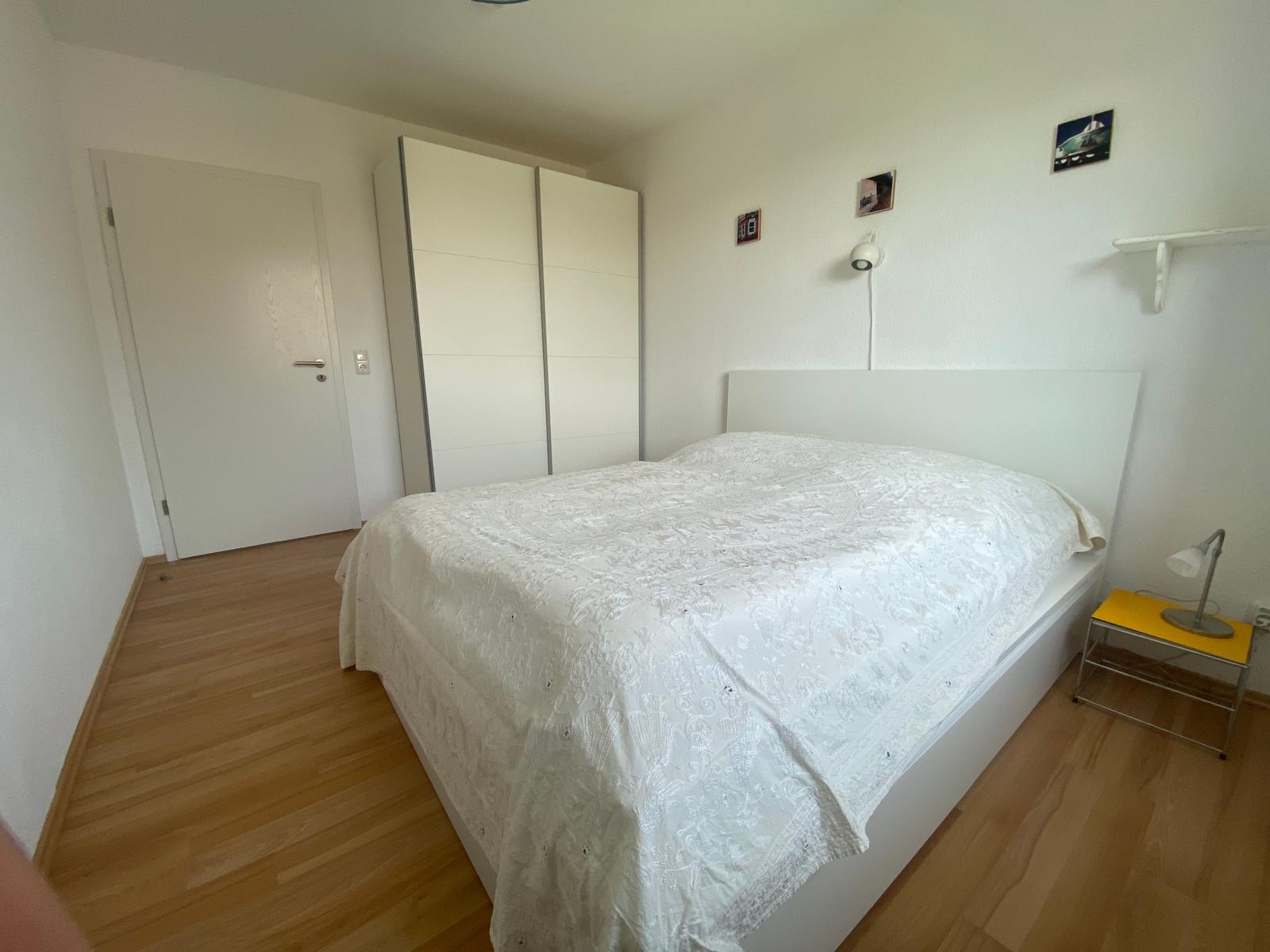 Schlafzimmer mit weißem Bett, Kleiderschrank und Nachttisch.