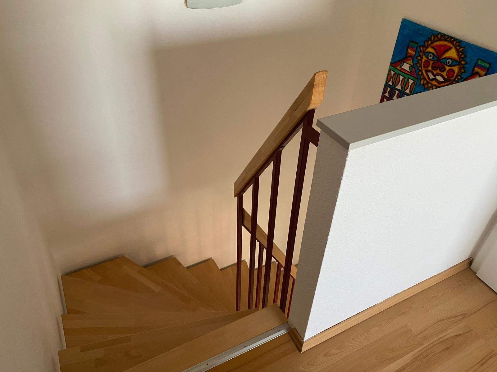 Holztreppe mit rotem Geländer und Wandbild an der Wand