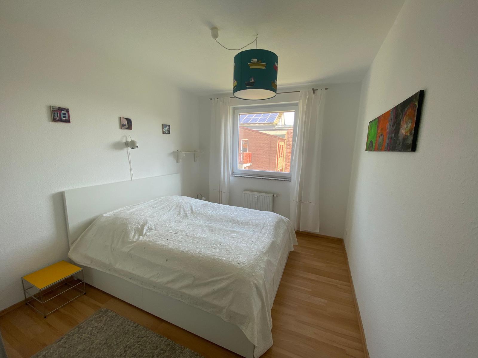 Schlafzimmer mit Bett, Fenster und Deckenleuchte.