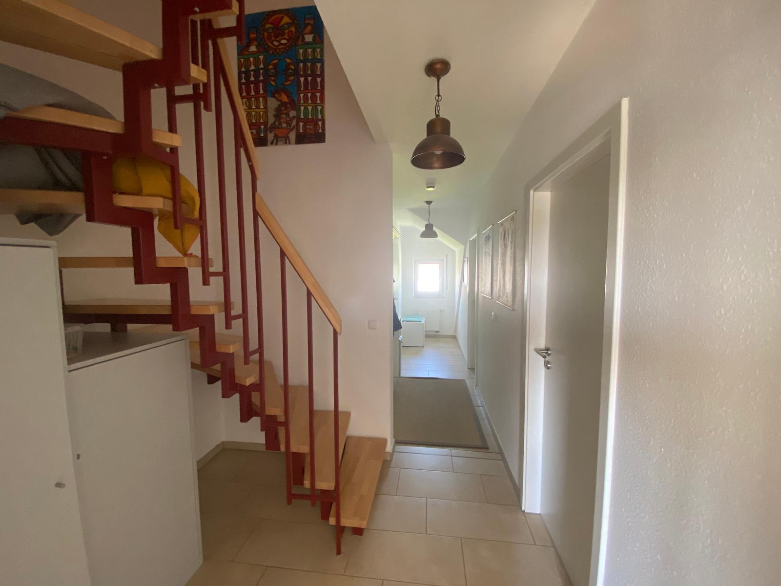 Hausflur mit roter Treppe und Wandbild. Flur führt in Wohnbereich.