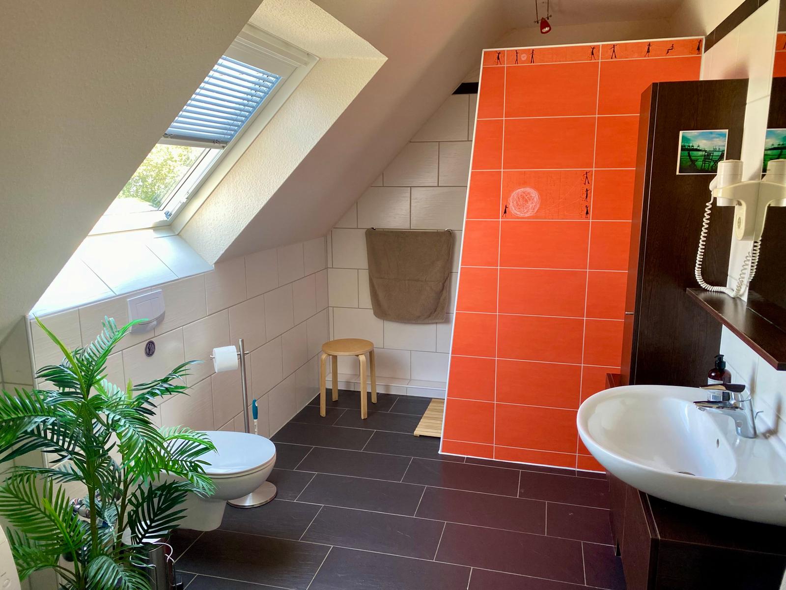 Badezimmer mit Dusche, Toilette und Waschbecken unter Dachschrägen.