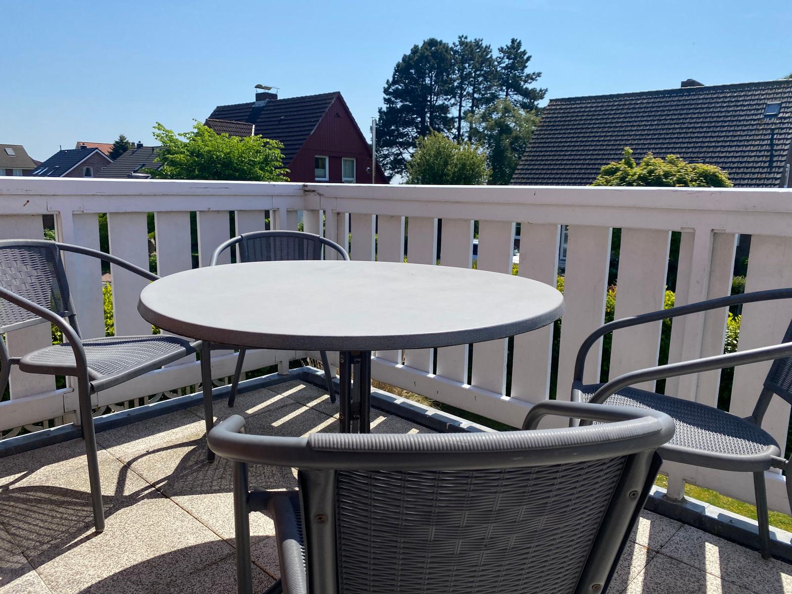 Terrasse mit runden Tisch und vier Stühlen, weißer Geländer und Blick auf Häuser.