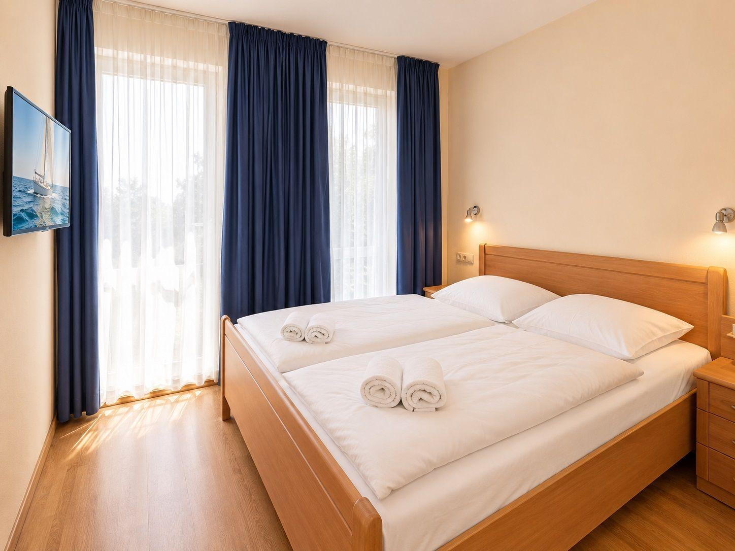 Bedroom with double bed, blue curtains, and TV mounted on the wall.