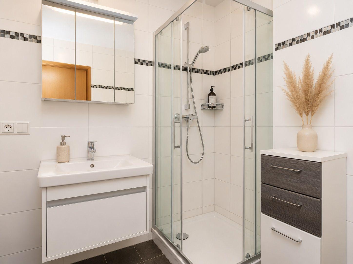 Bathroom with shower, sink, and cabinet. Tiles and glass wall visible.