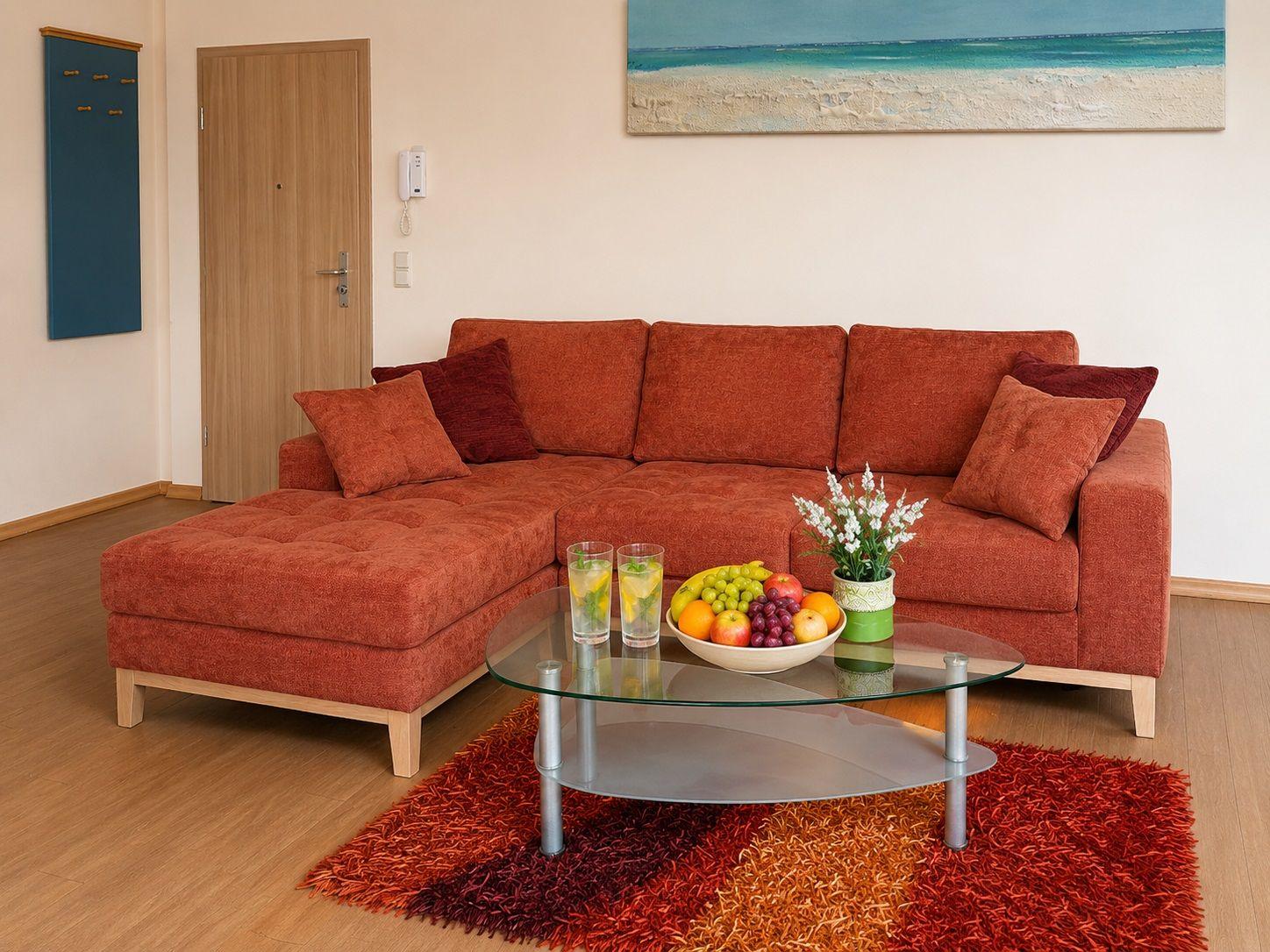 A living room with a red sofa, a glass table, and a colorful rug.