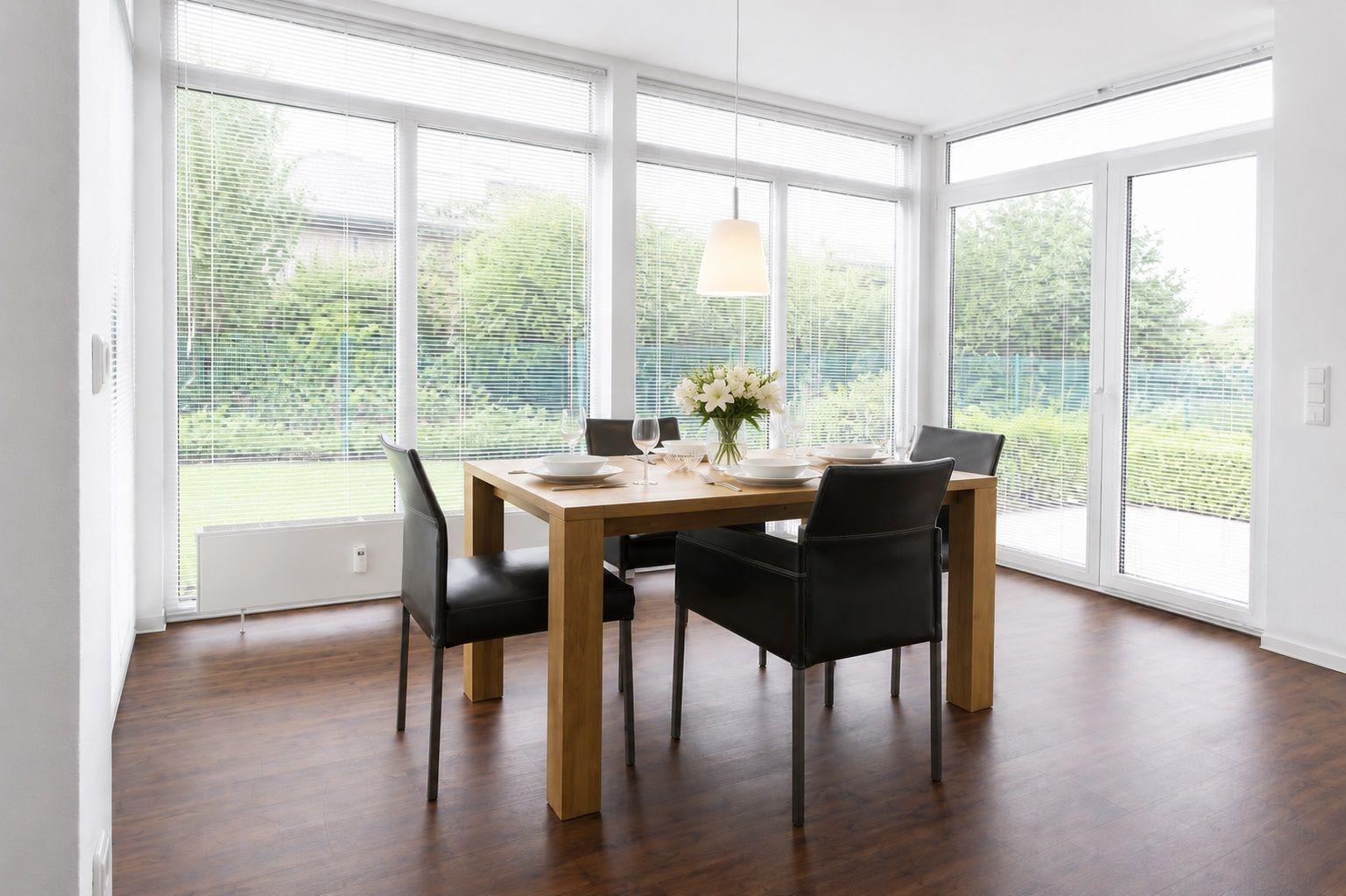 Esszimmer mit Holztisch, schwarzen Stühlen und großen Fenstern zur grünen Außenansicht.