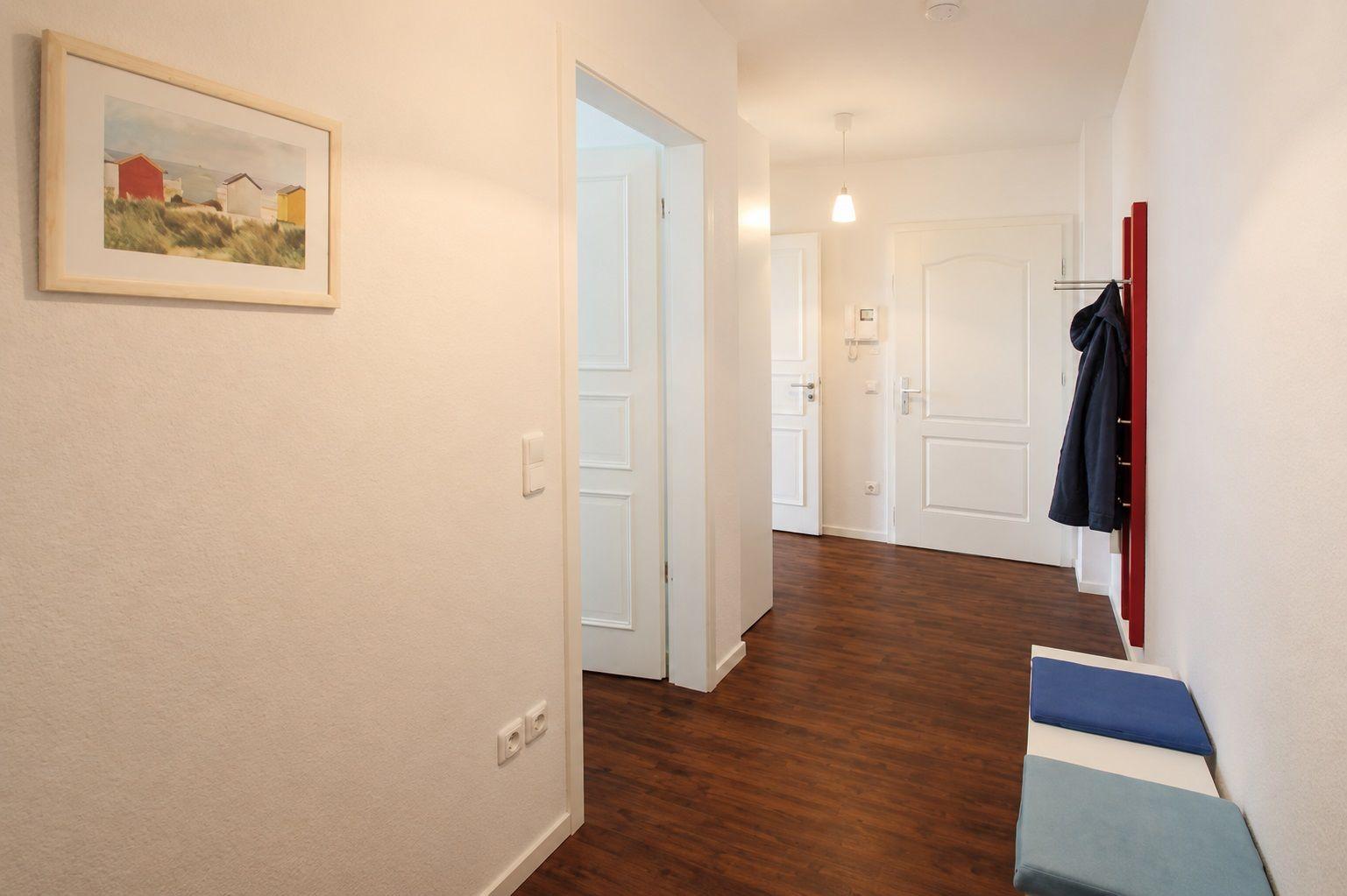 Flur mit Holzboden, weißen Türen und rotem Garderobenständer mit Jacke.