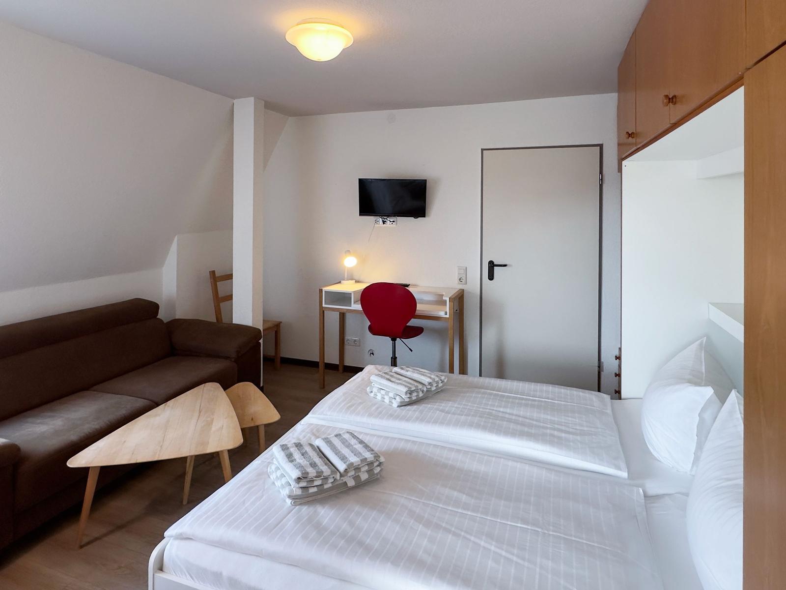 Ein Schlafzimmer mit Doppelbett, Sofa, Schreibtisch und Fernseher.