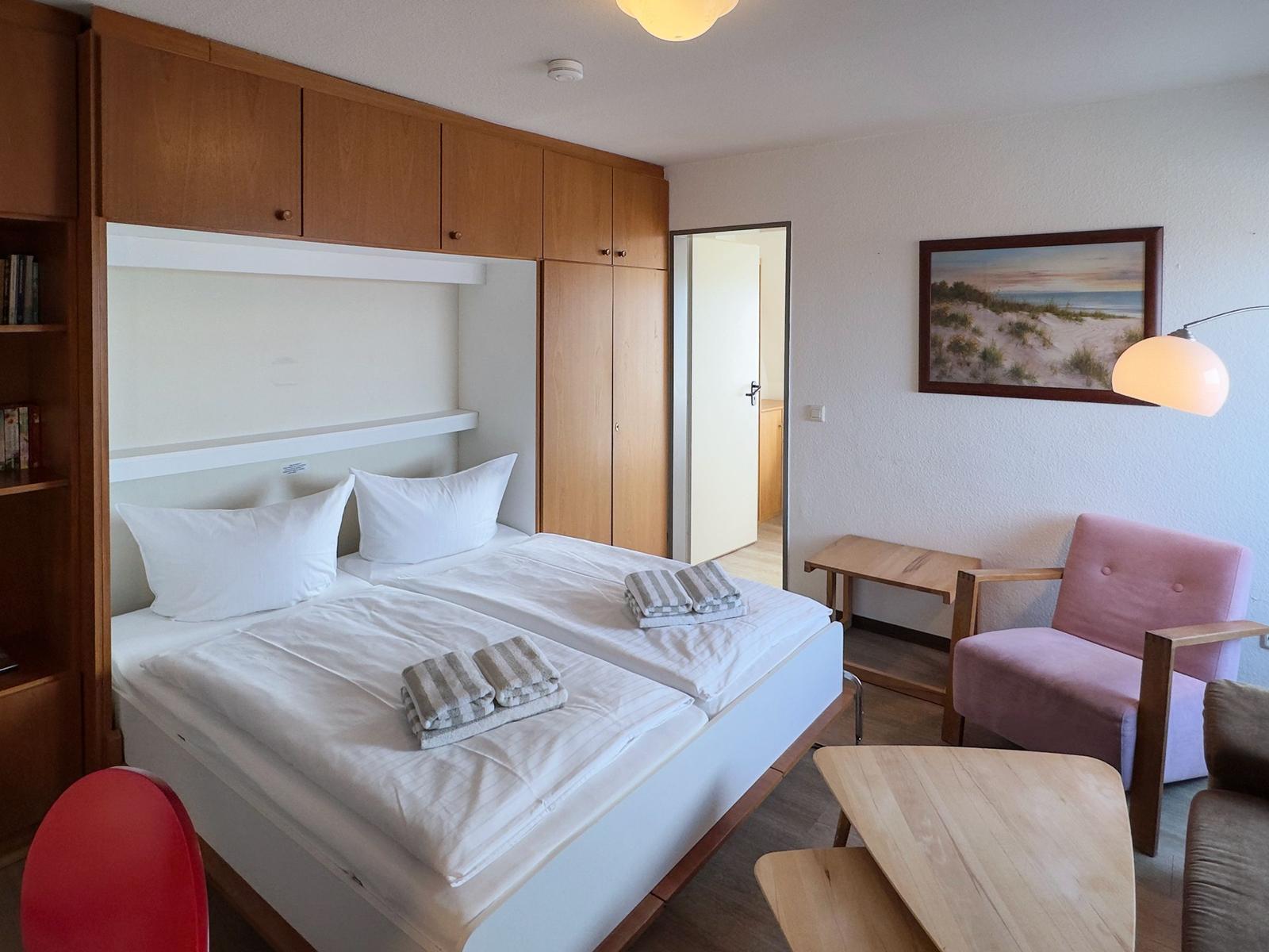 Schlafzimmer mit Doppelbett, Holzmöbeln und rosa Sessel.