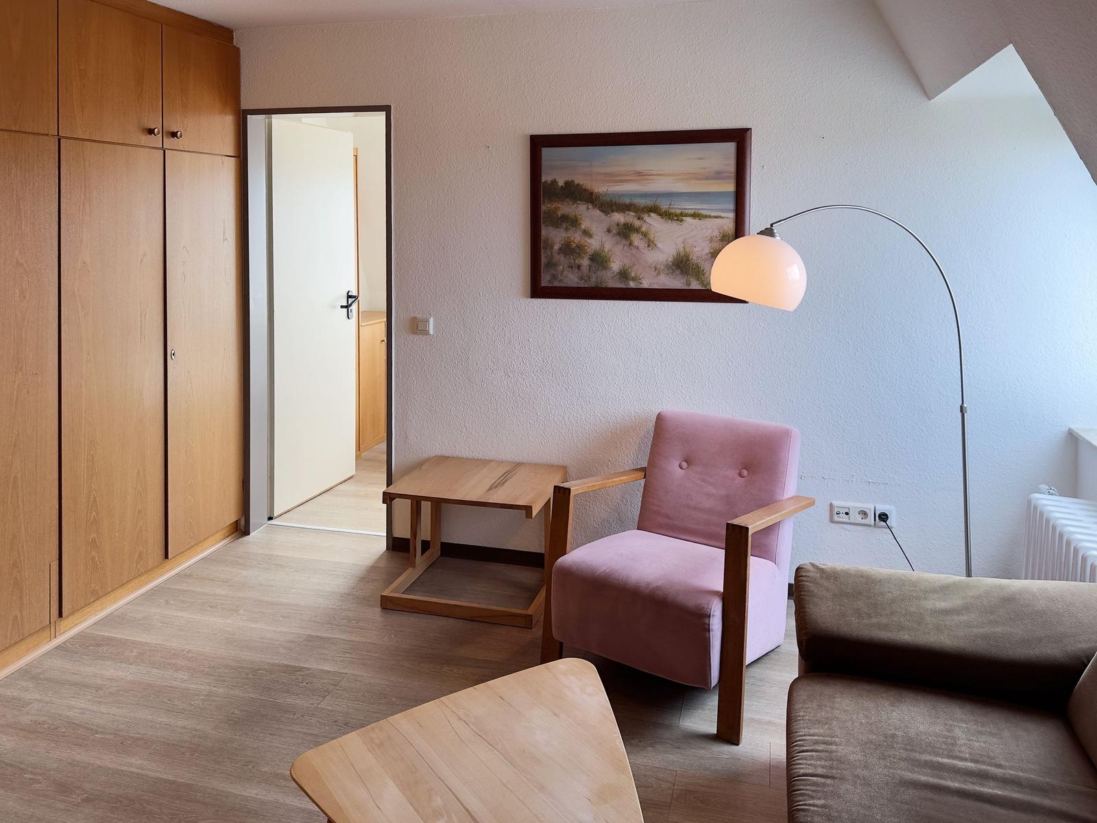 Ein Raum mit Holzmöbeln, einem rosa Sessel und einer Wandlampe.