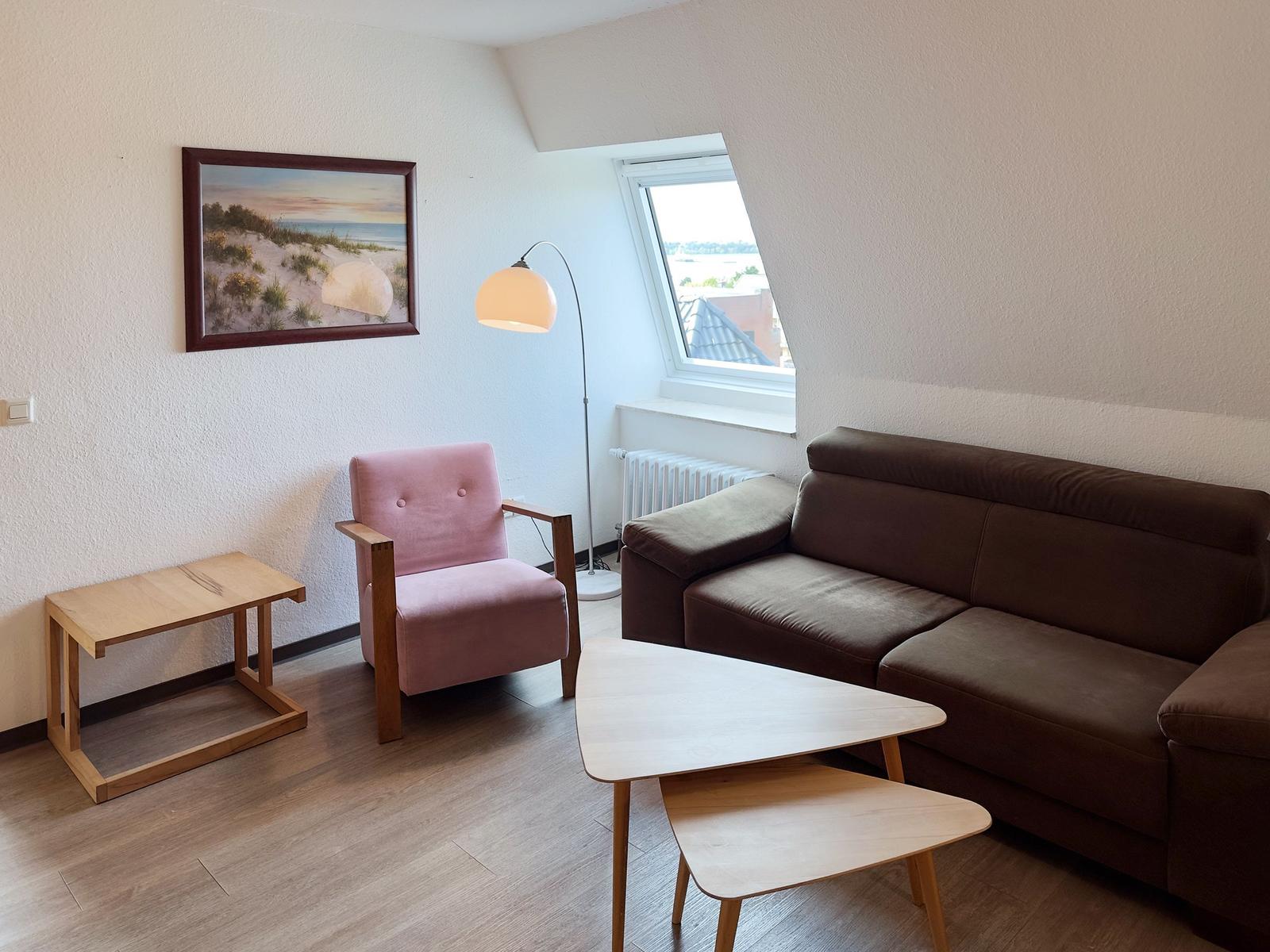 Wohnzimmer mit braunem Sofa, rosa Sessel, Tisch und Fenster