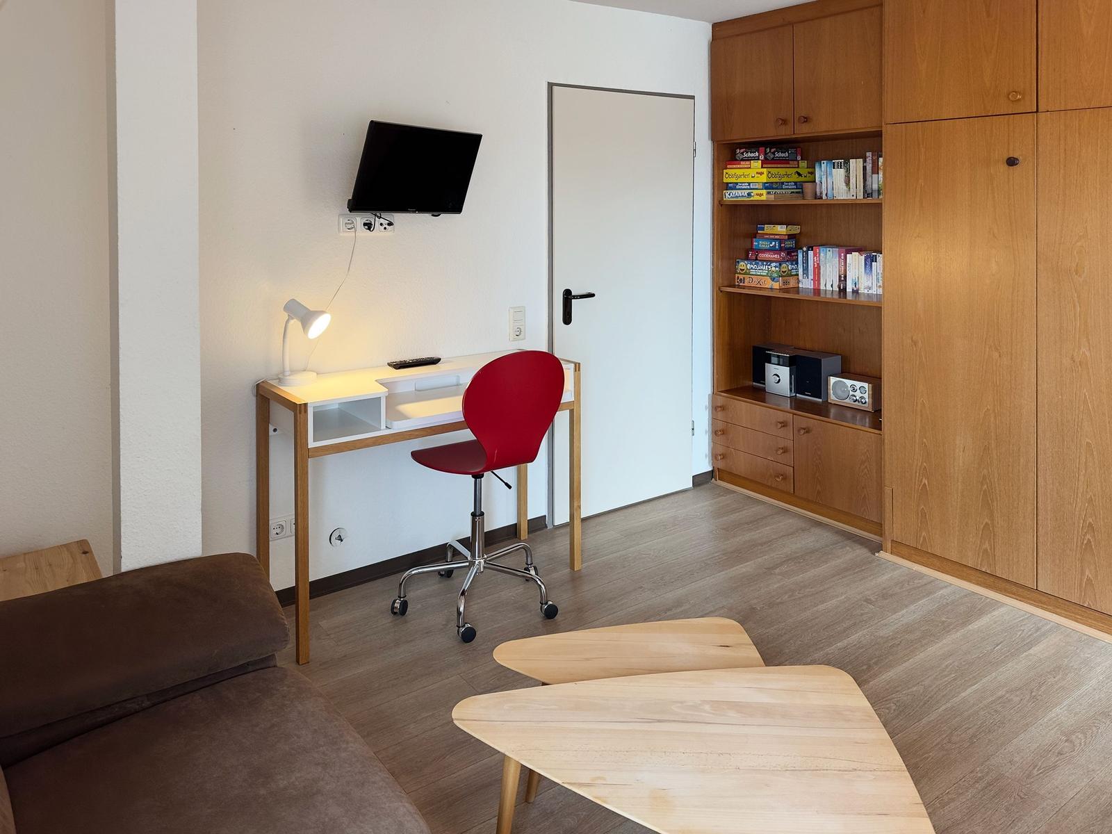 Ein Raum mit Schreibtisch, roter Stuhl, TV und Holzmöbel.