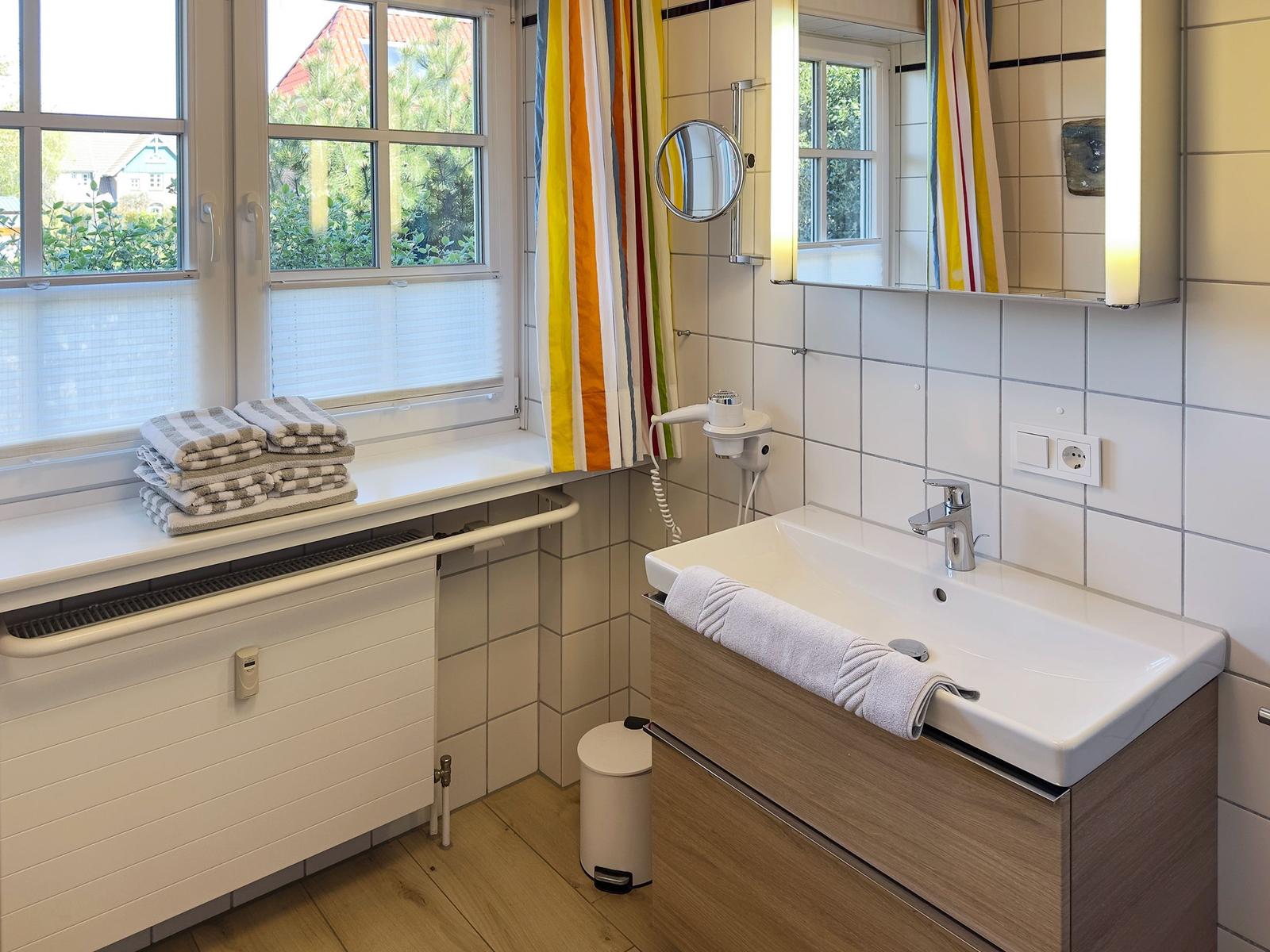 Badezimmer mit Waschbecken, Spiegel und Fenster mit Blick auf Garten.