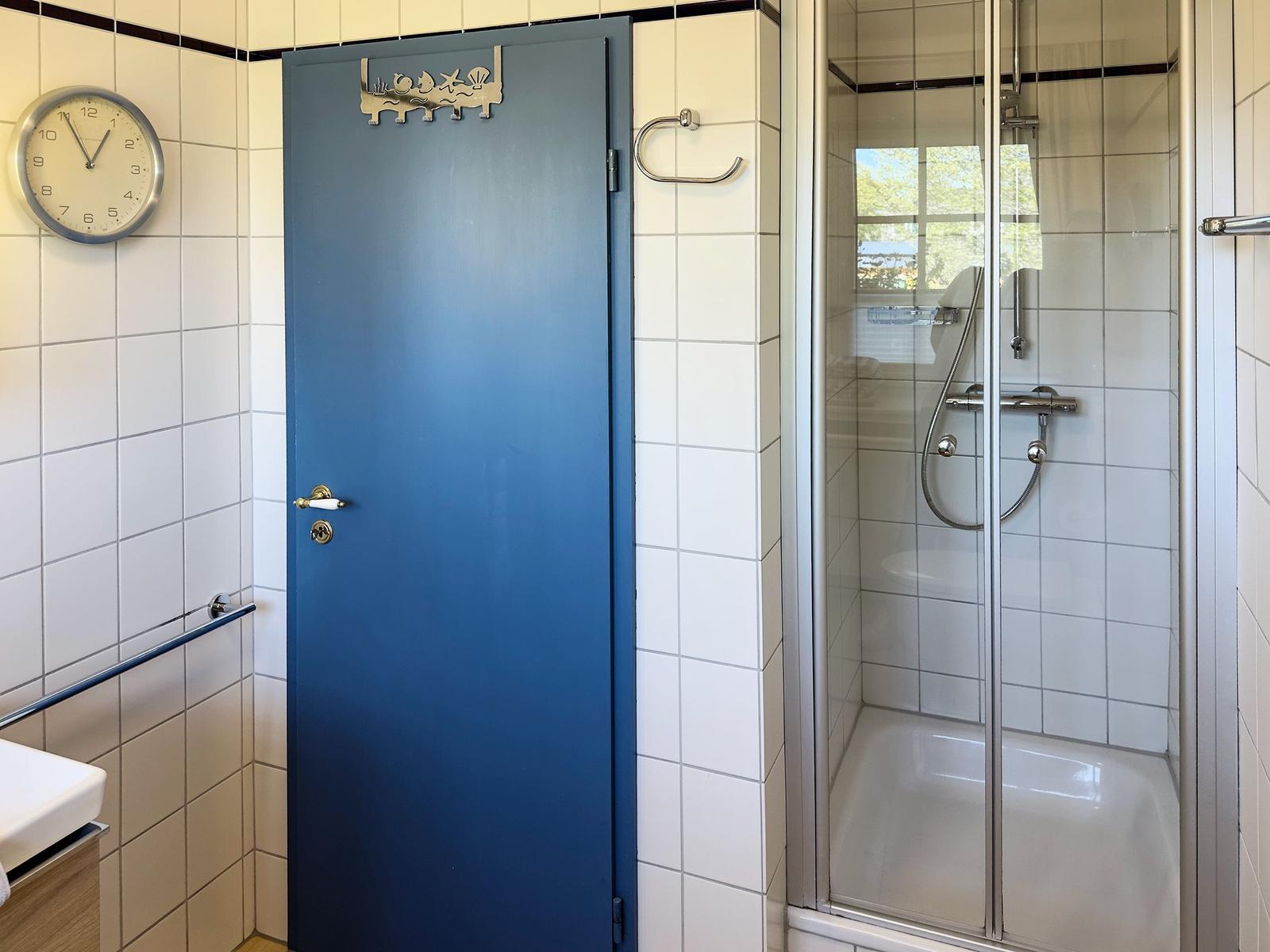 Badezimmer mit Dusche, blauer Tür und Wanduhr.