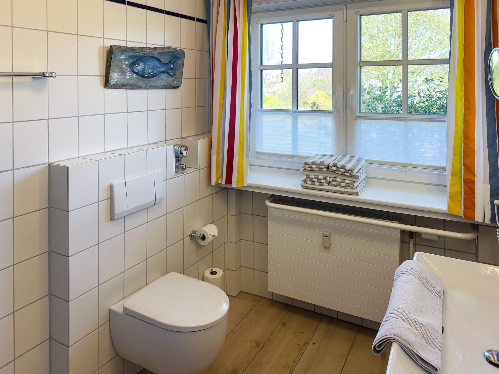 Badezimmer mit Toilette, Waschbecken und Fenster mit bunten Vorhängen.