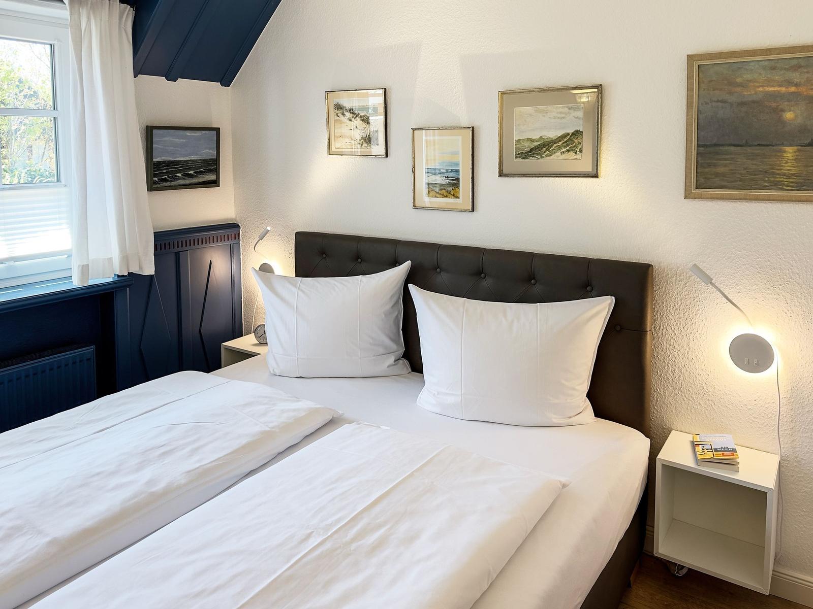 Schlafzimmer mit Doppelbett, Wandbildern und Nachttischen mit Lampen.
