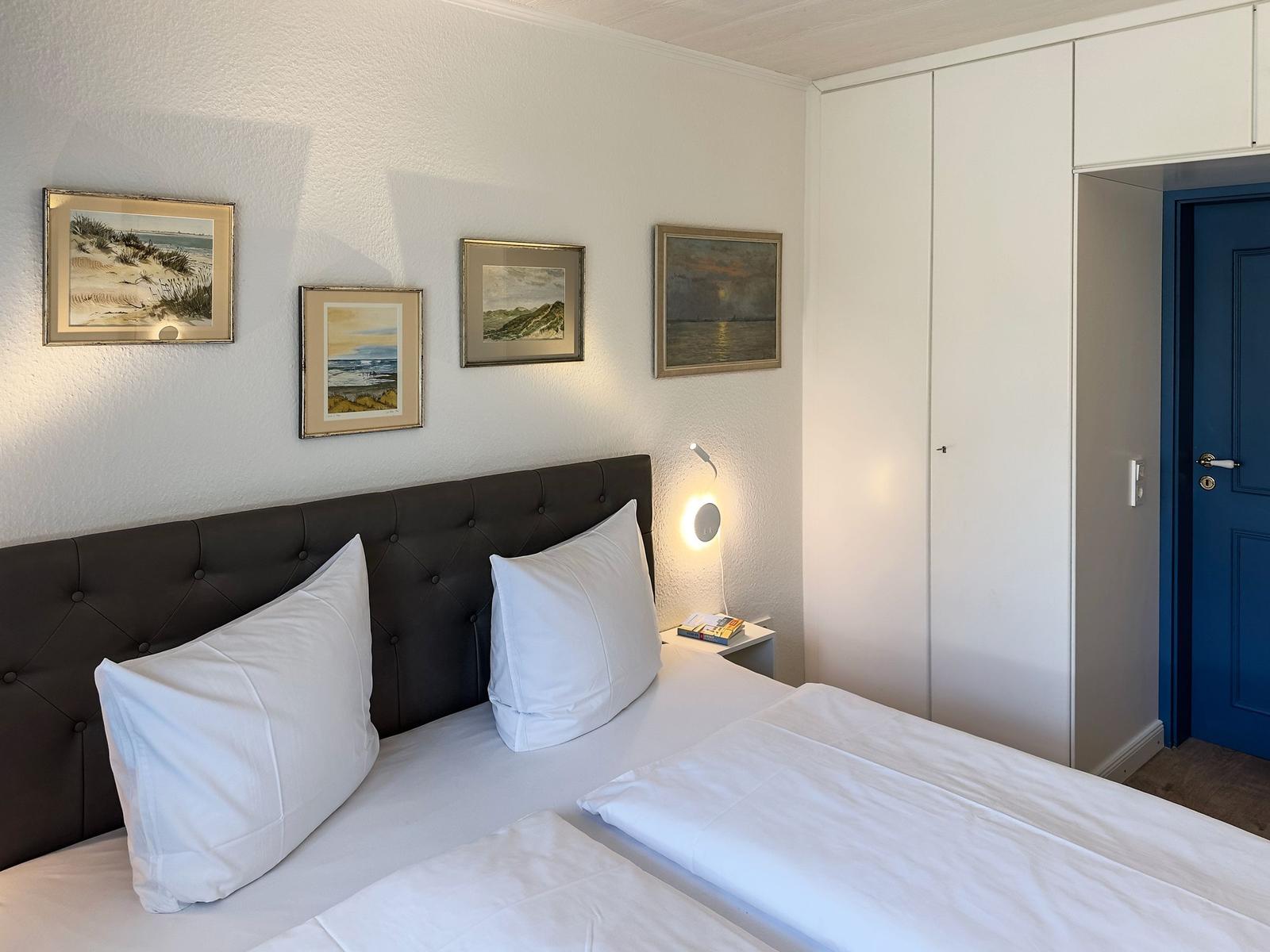 Schlafzimmer mit Doppelbett, weißen Bettwäsche, Wandbildern und Schrank.