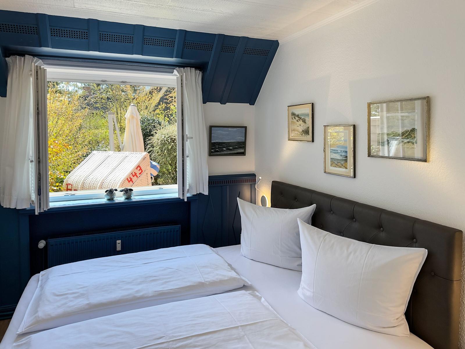 Schlafzimmer mit Bett, Fenster und Wandbildern.