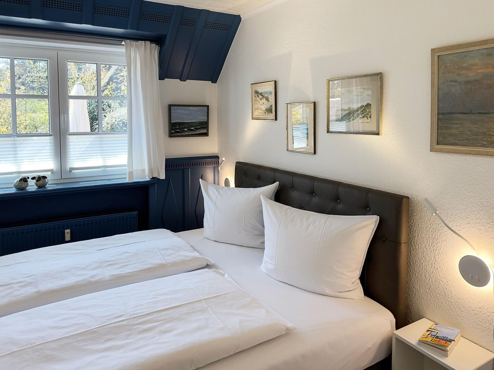 Schlafzimmer mit Doppelbett, Fenster und Wandbildern.