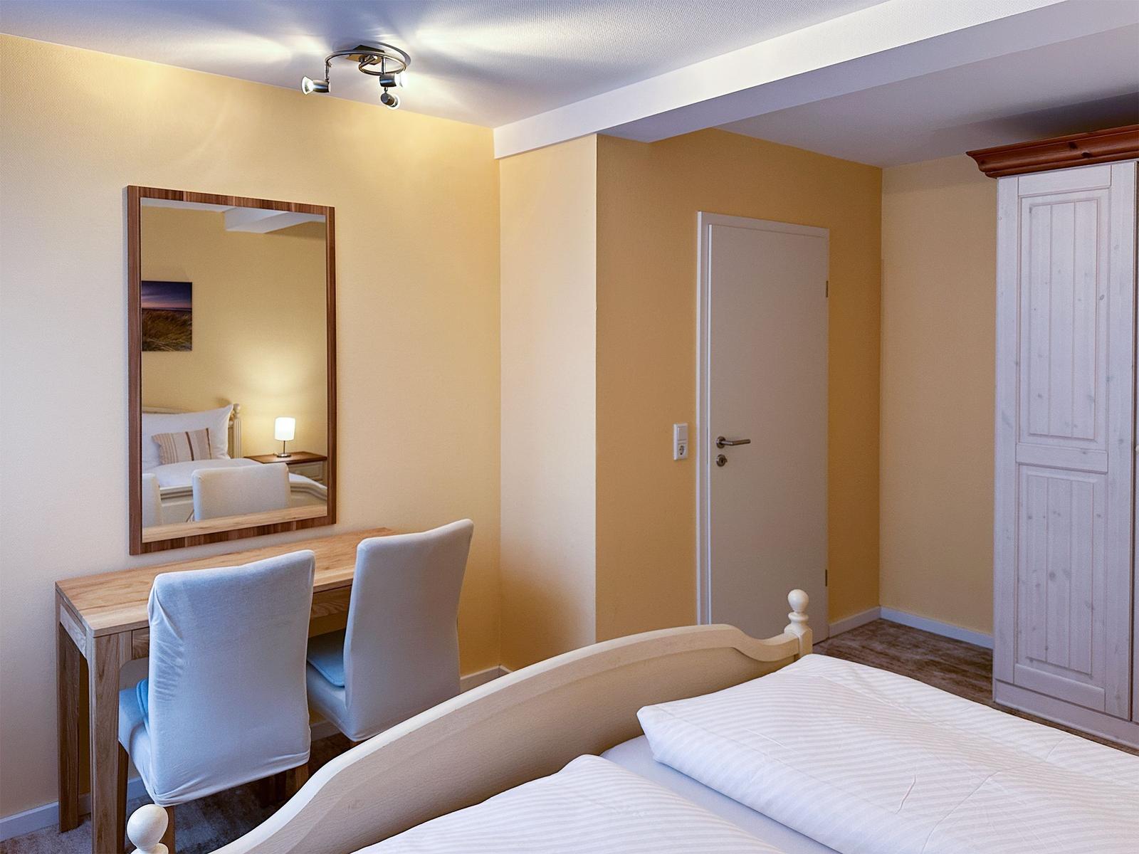 Schlafzimmer mit Bett, Schreibtisch, Spiegel und Kleiderschrank.