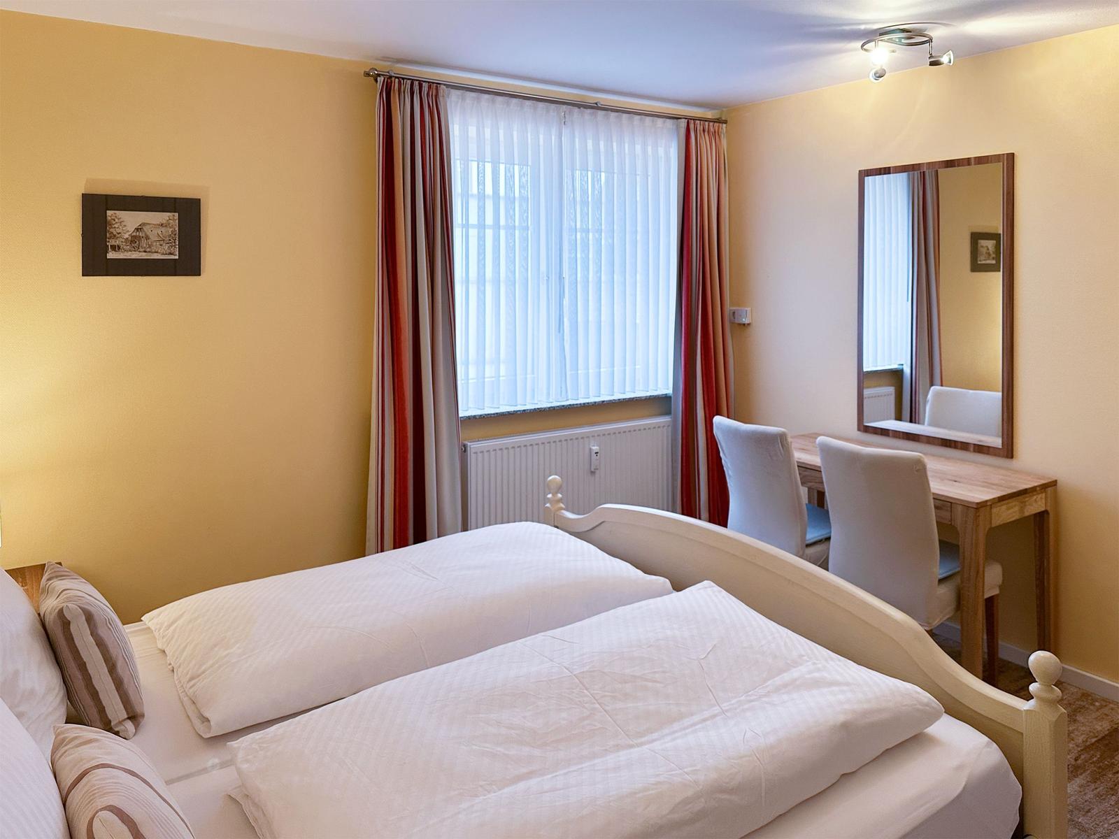 Zimmer mit Doppelbett, Schreibtisch und Spiegel an der Wand.
