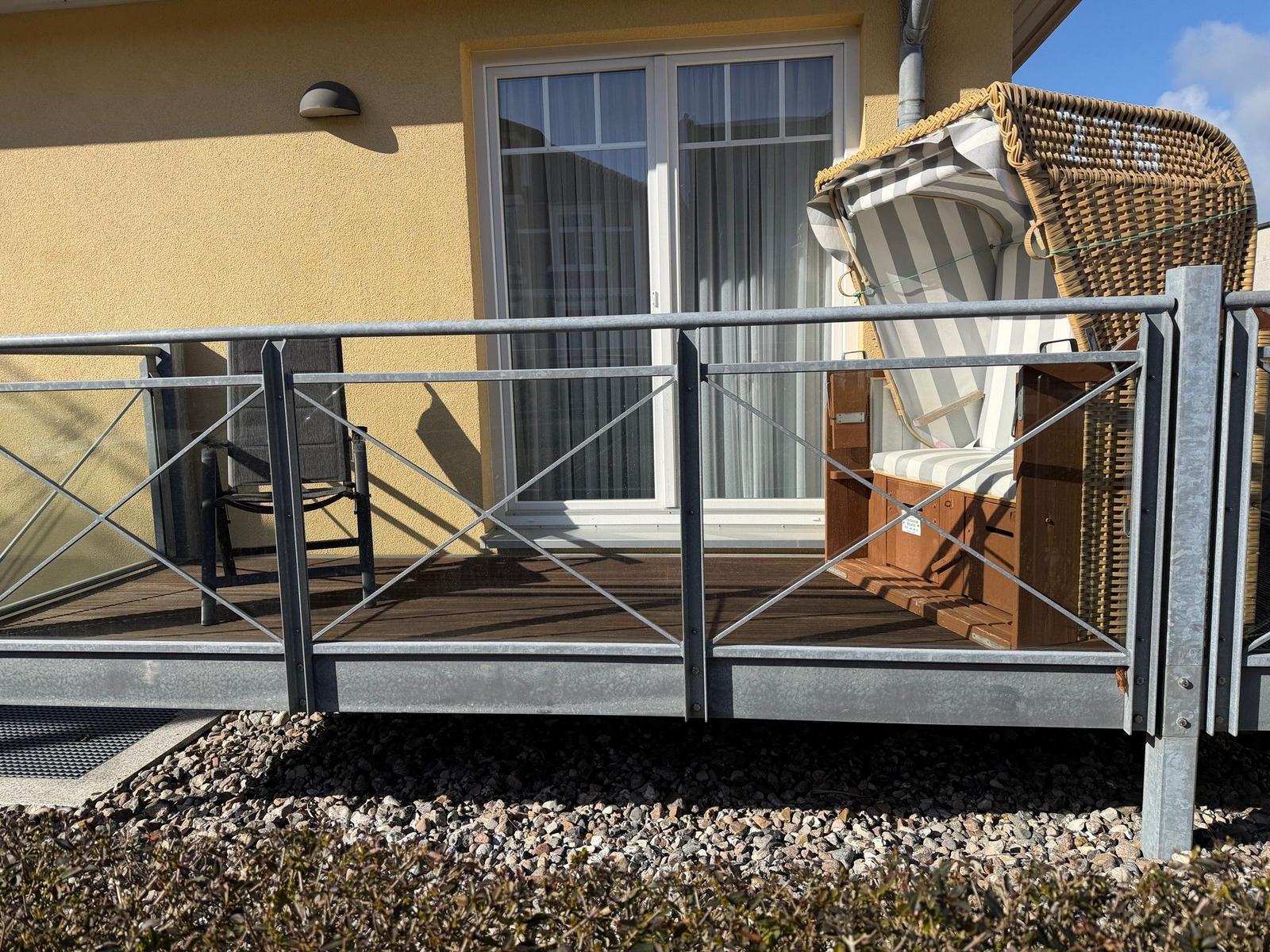 Terrasse mit Hängesessel und Gittergeländer vor gelbem Haus mit Fenster.