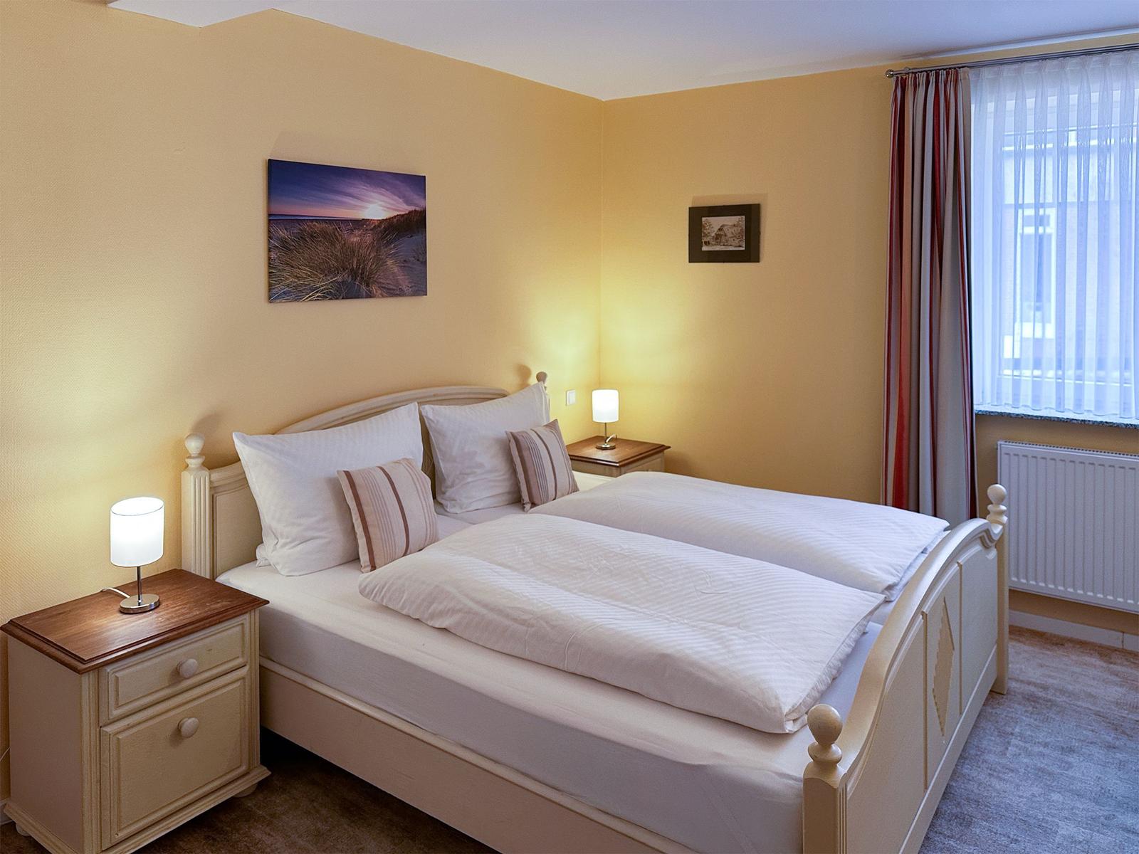 Ein Schlafzimmer mit Doppelbett, zwei Nachttischen und einem Fenster mit Vorhängen.