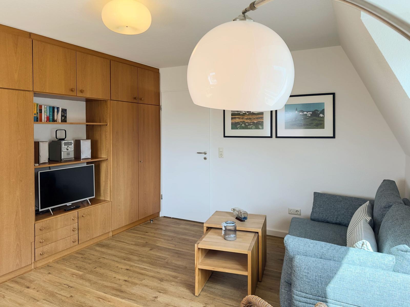 Living room with sofa, wooden furniture, and TV under sloped ceiling.
