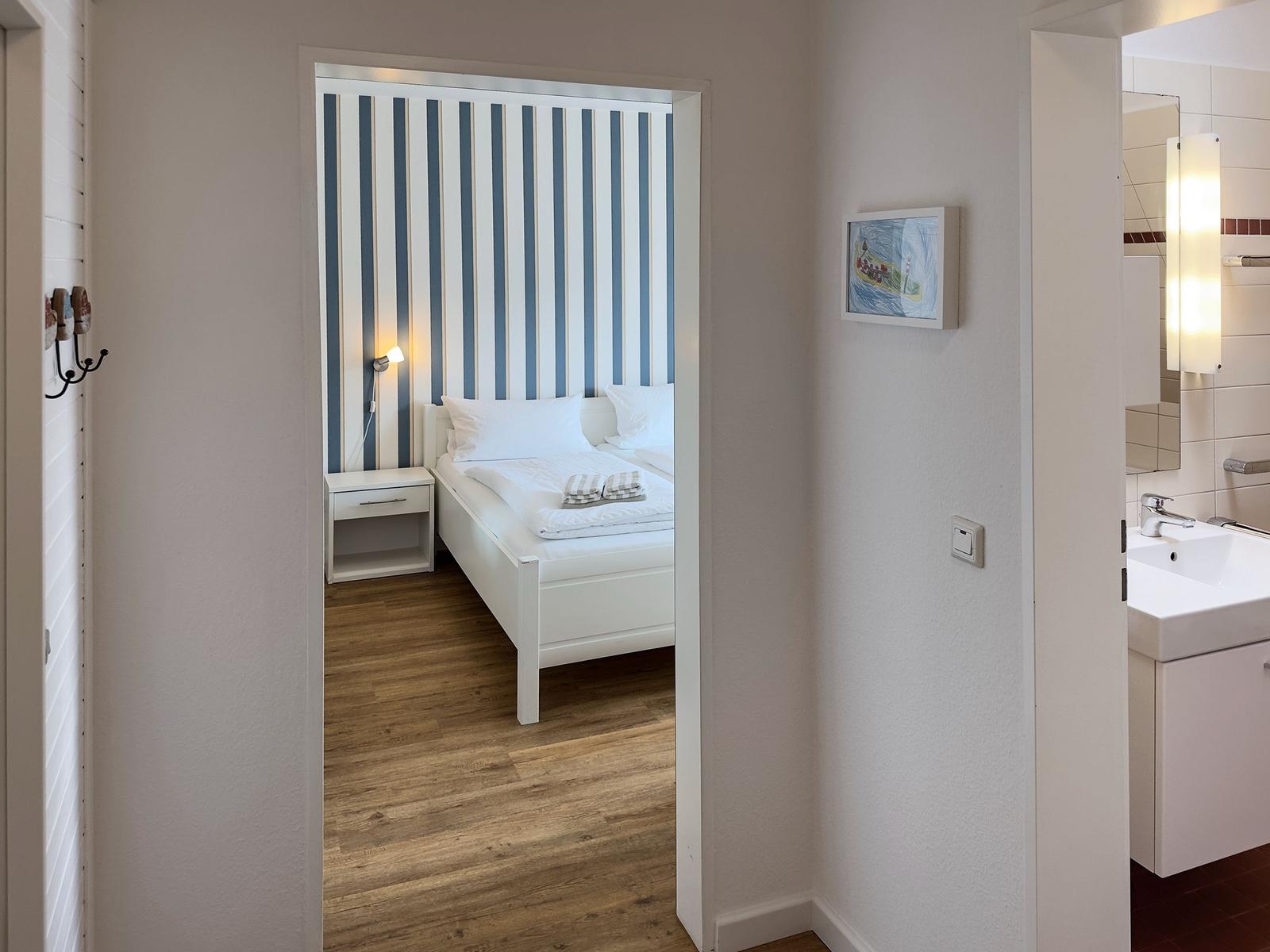 Bedroom with bed and striped wall. Adjacent room with sink.
