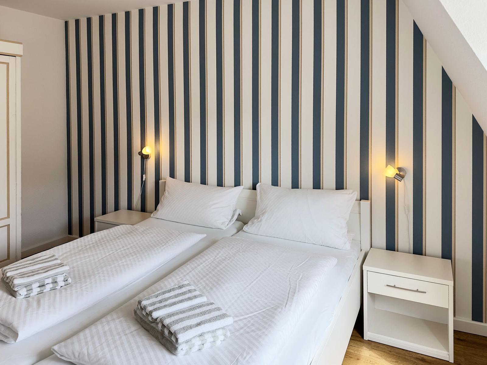 Two beds with white bedding and striped towels against a striped wall.