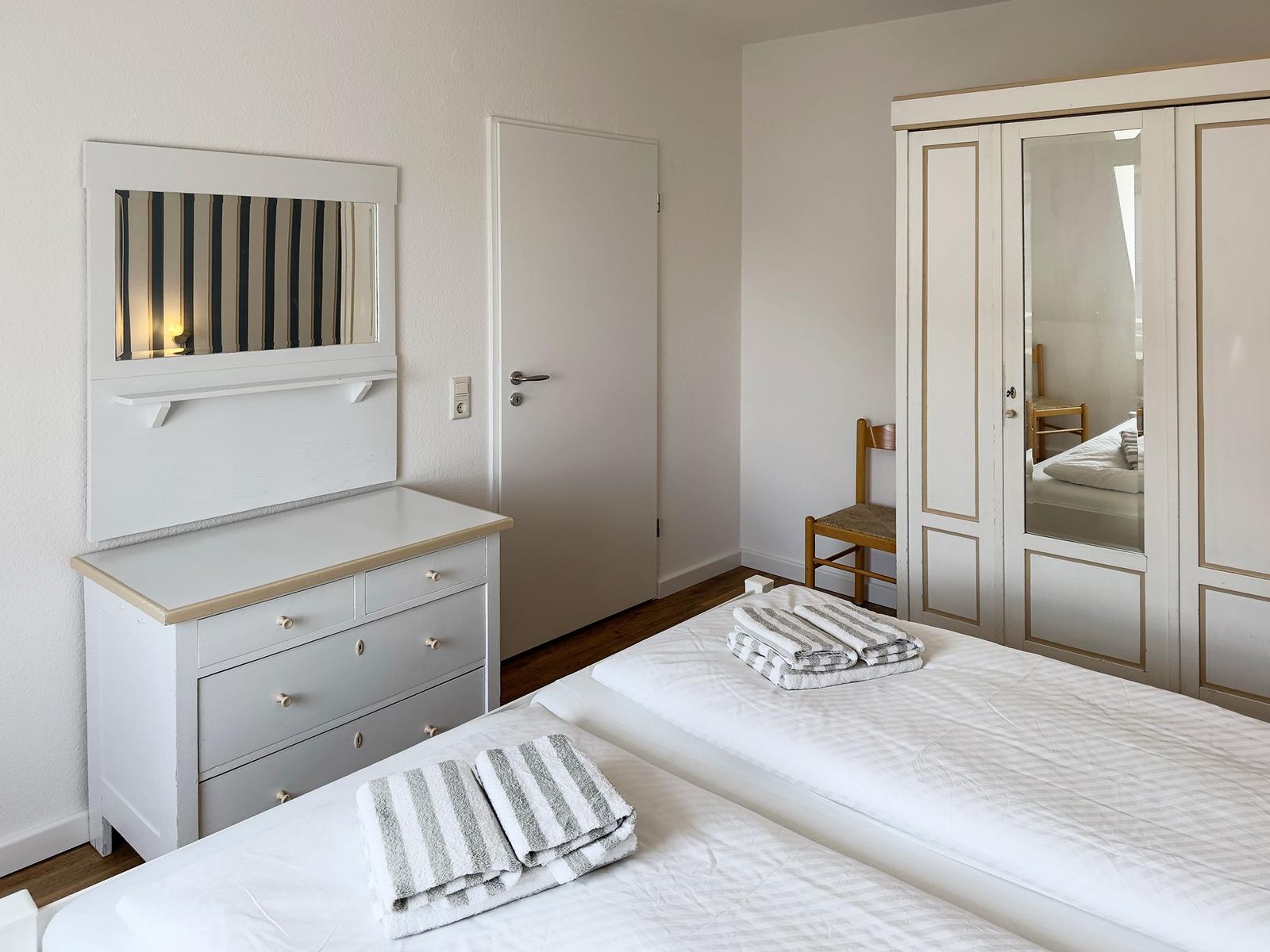Two beds with towels, wardrobe with mirrored doors, and vanity with mirror.