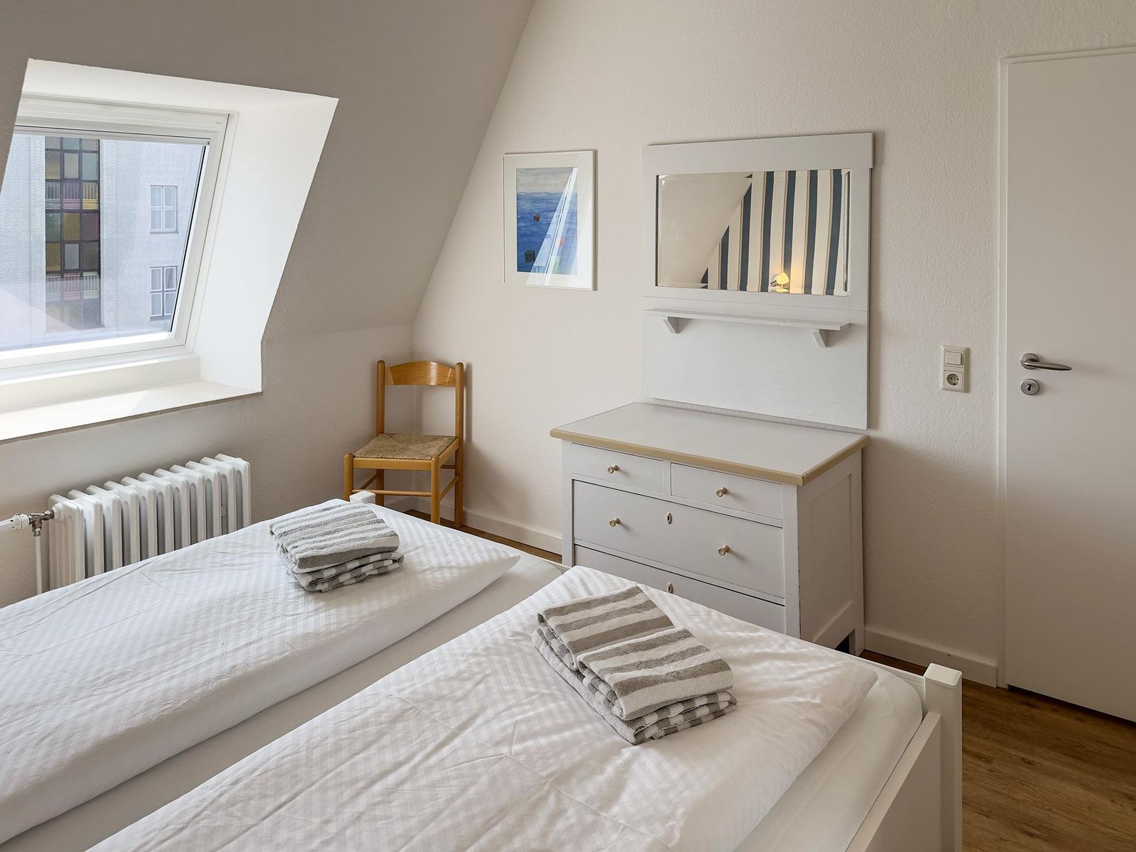 Room with two beds, dresser, and skylight. Wooden chair and radiator are present.