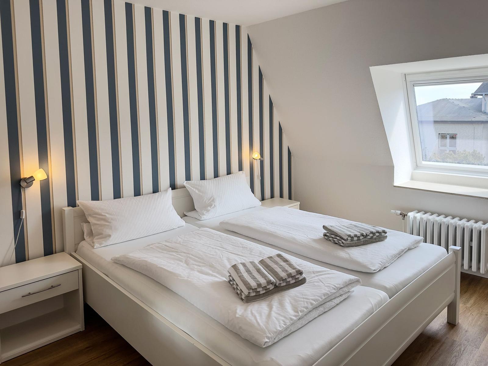 Room with two beds, striped wall, and skylight.