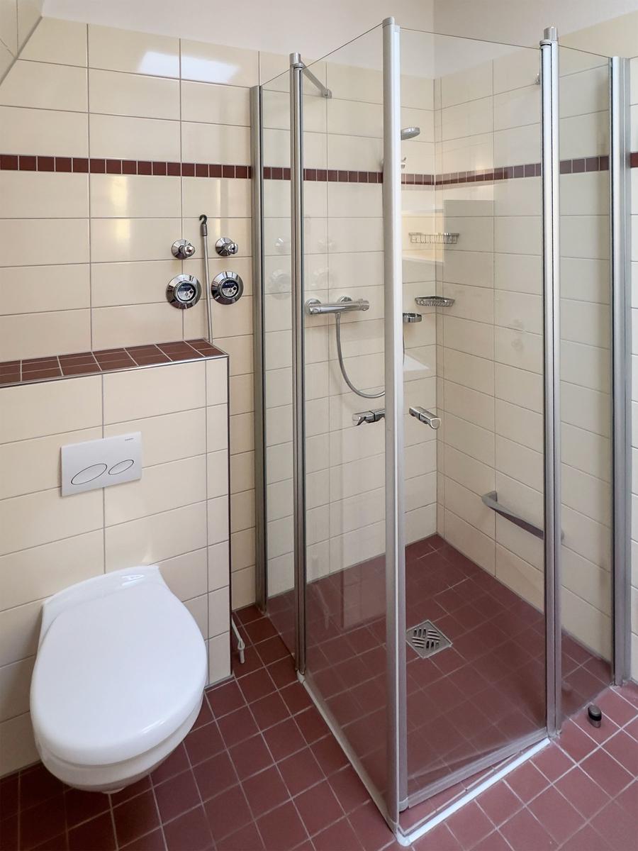 Bathroom with shower, toilet, and tiled floor.