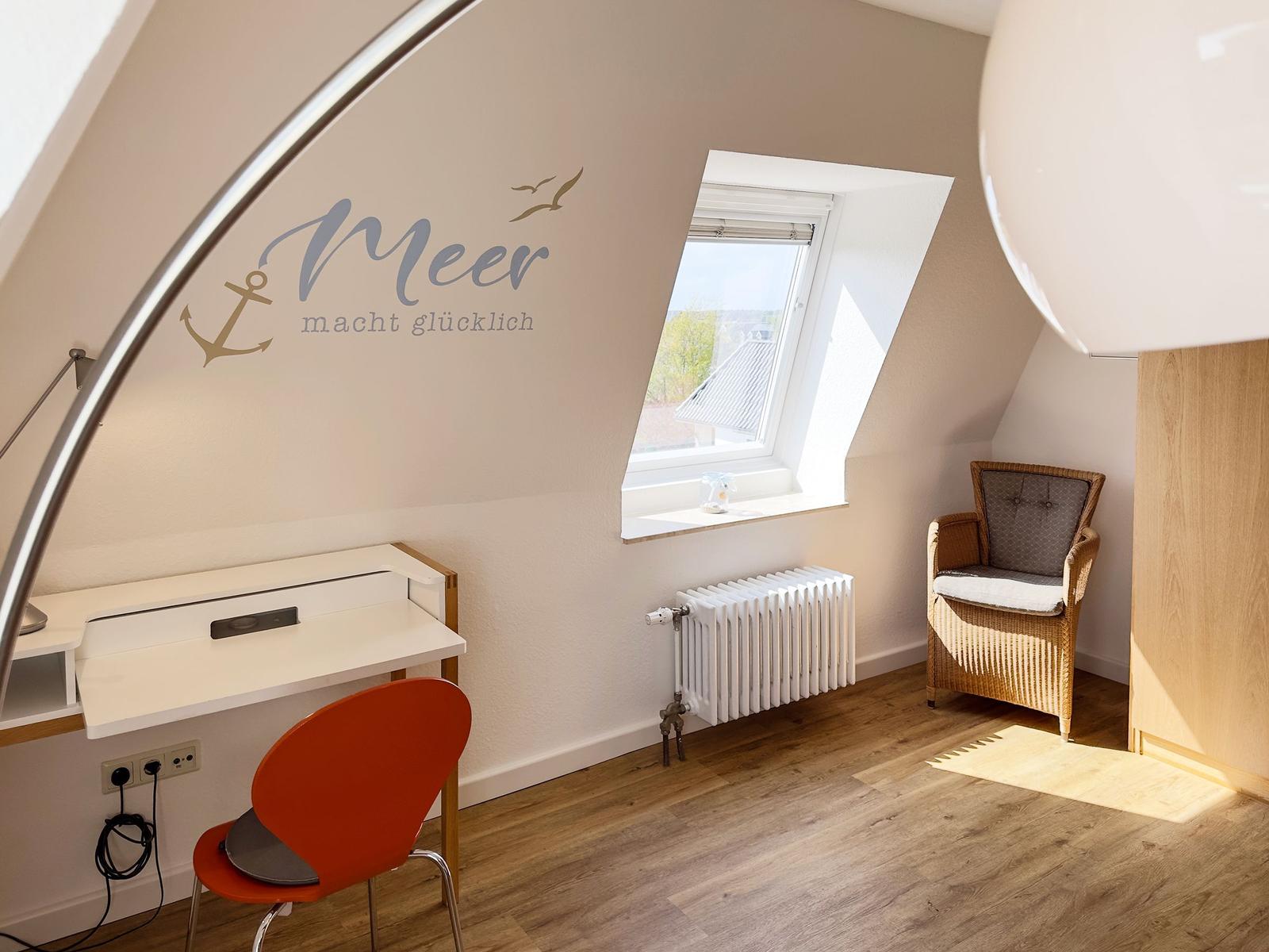 Bedroom with desk, chair, and armchair under sloped ceilings. Wall decoration with sea motif.