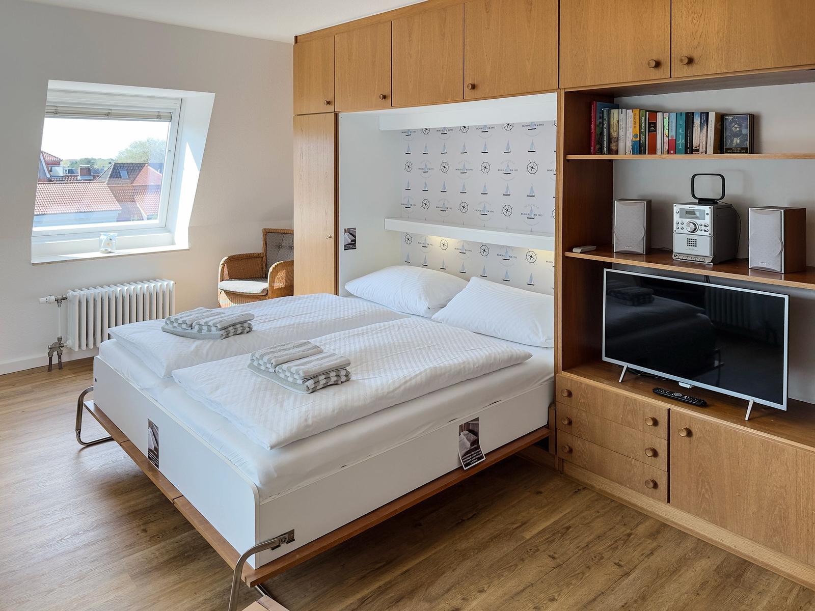 Bedroom with double bed, window, TV, and wooden furniture.