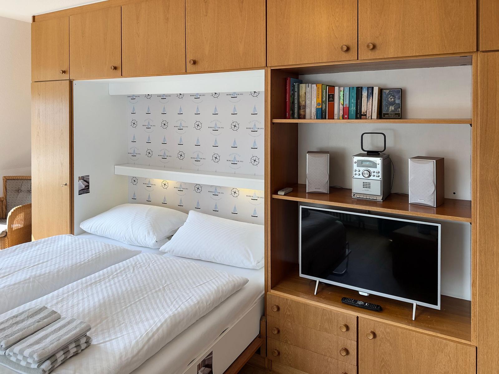 Bedroom with bed, bookshelf, and TV in wooden cabinet.
