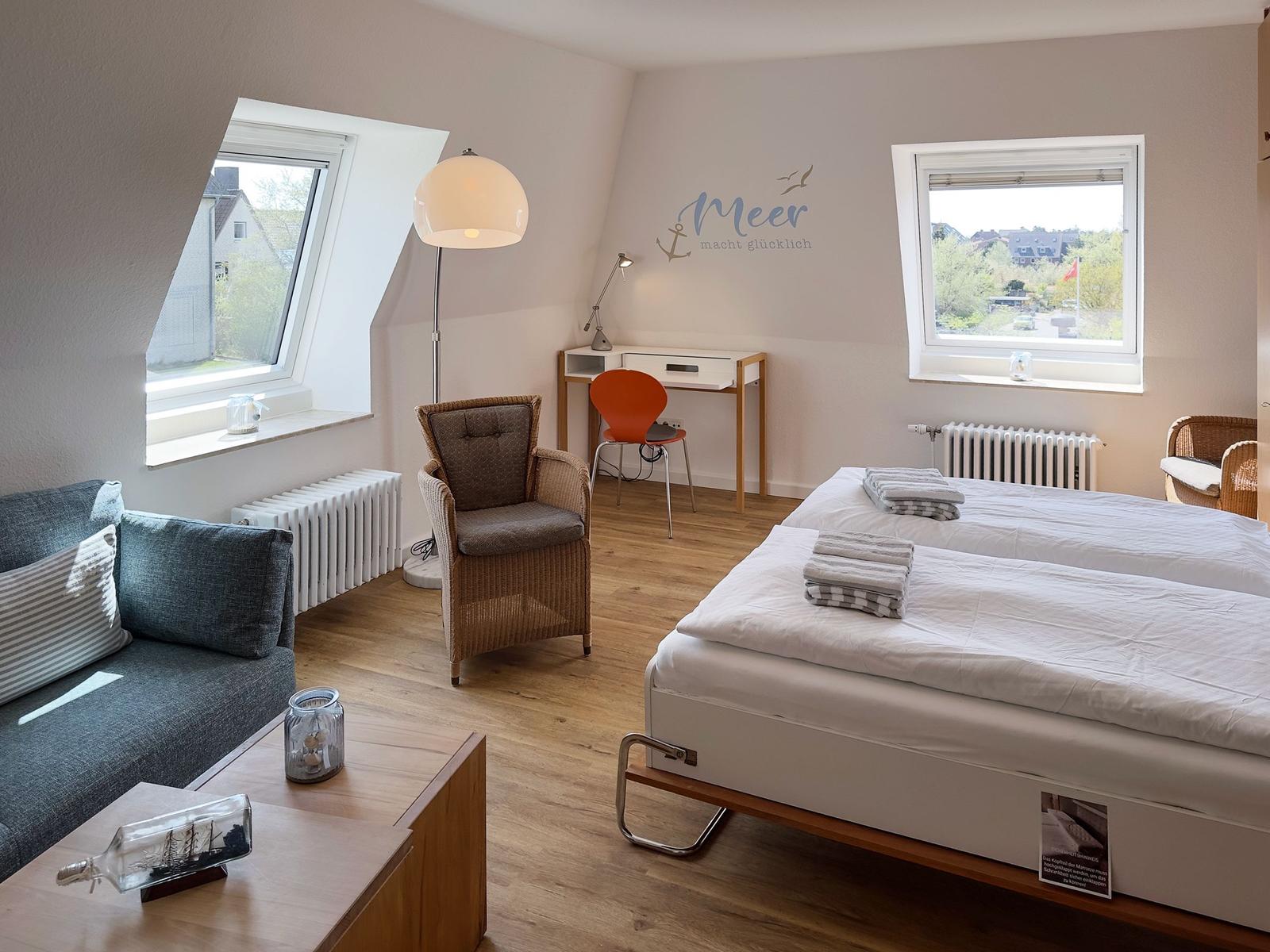 Room with double bed, sofa, desk, and two windows with views.