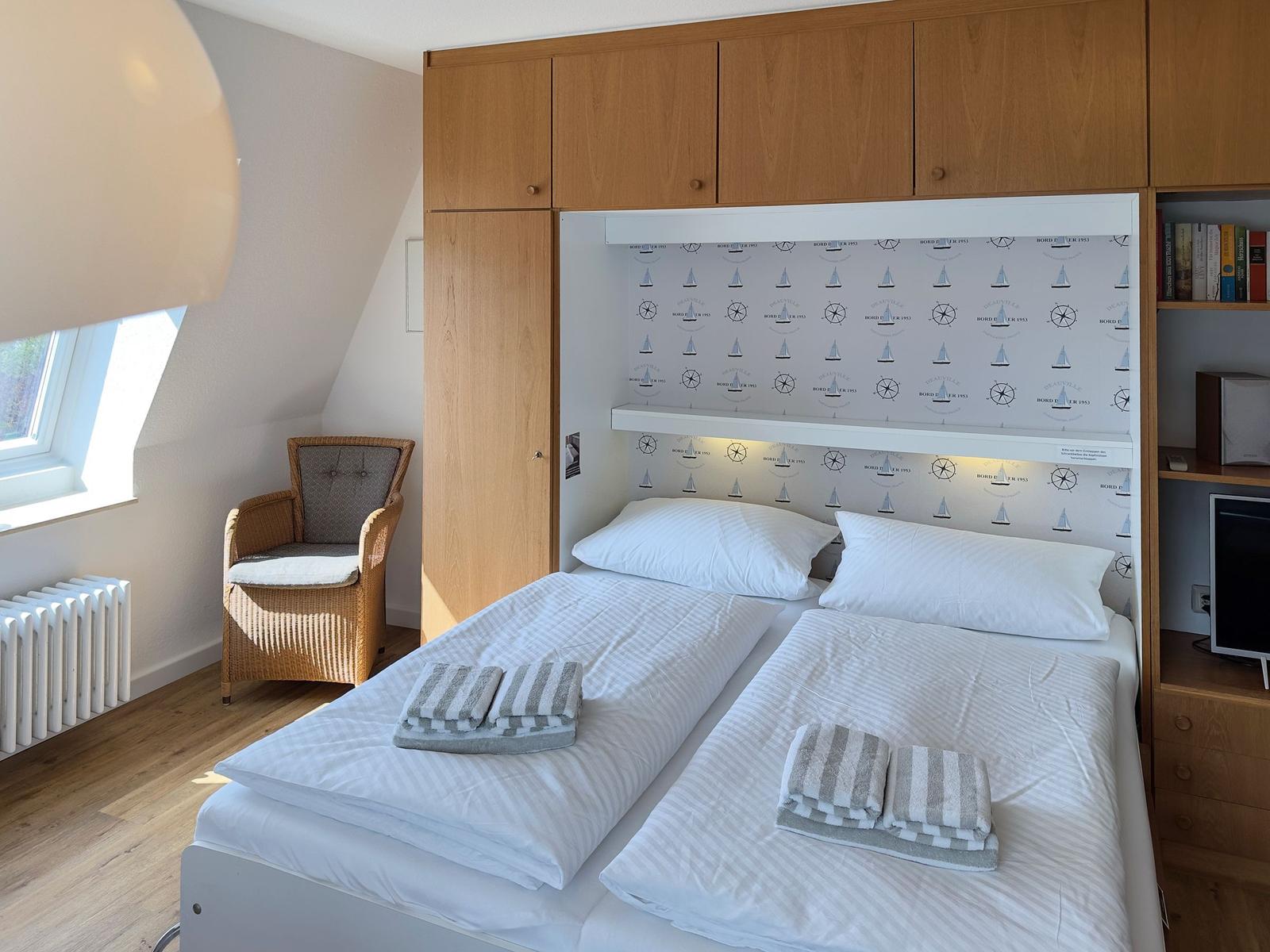 Two beds with white linens and towels. Wooden furniture and window.