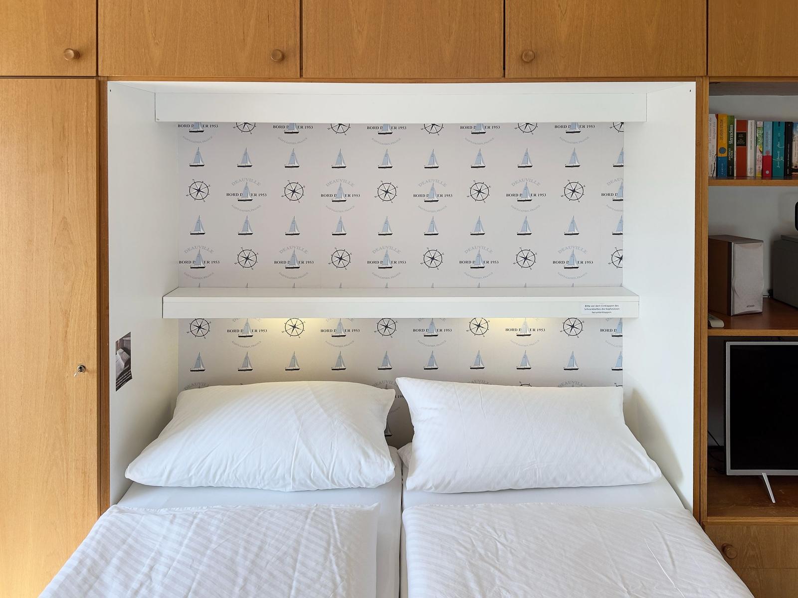 Two beds with white pillows and bedding under a wall panel with sailboat motif.
