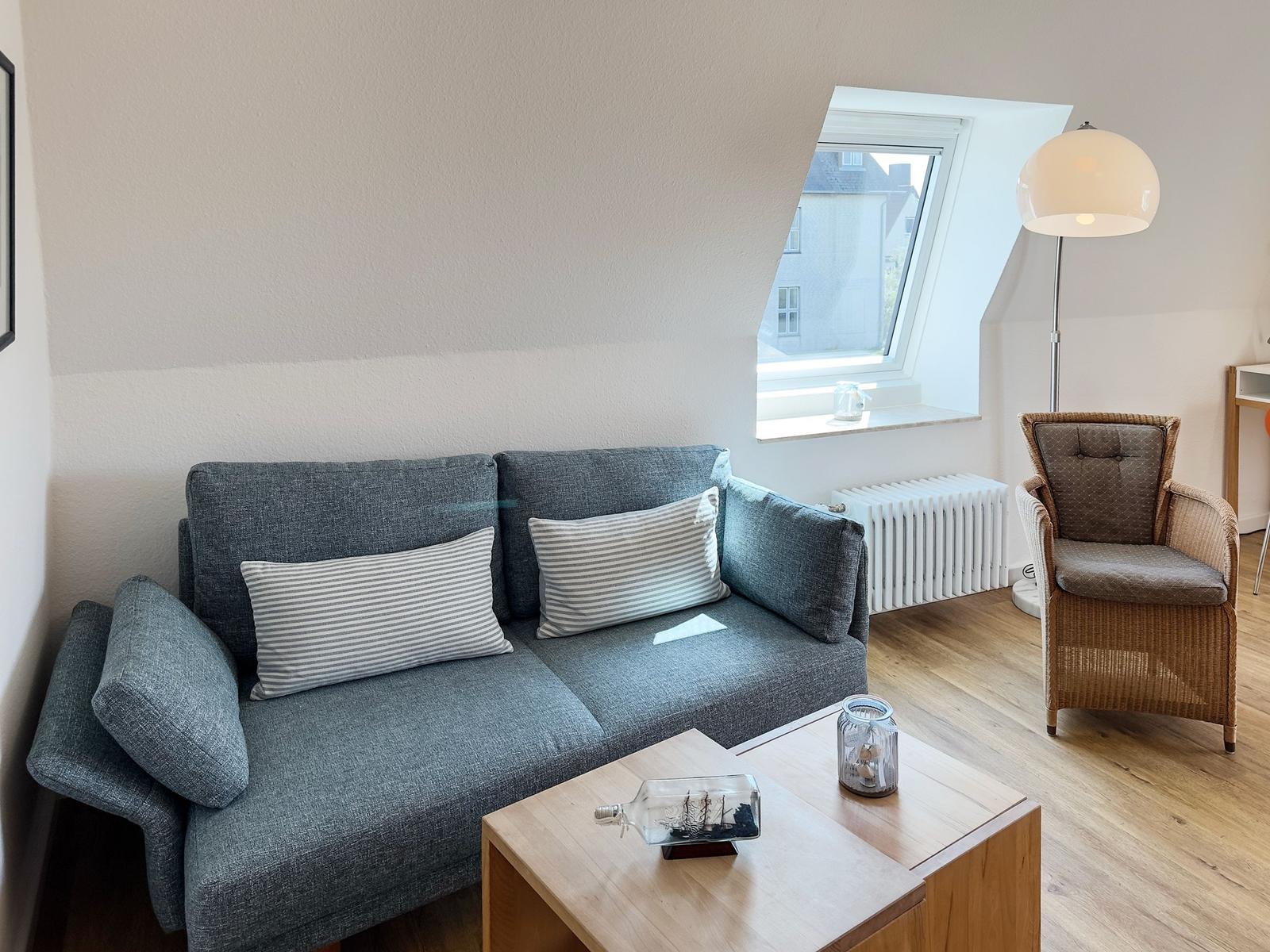 A living room with gray sofa, wooden table, and seating under sloped ceilings.