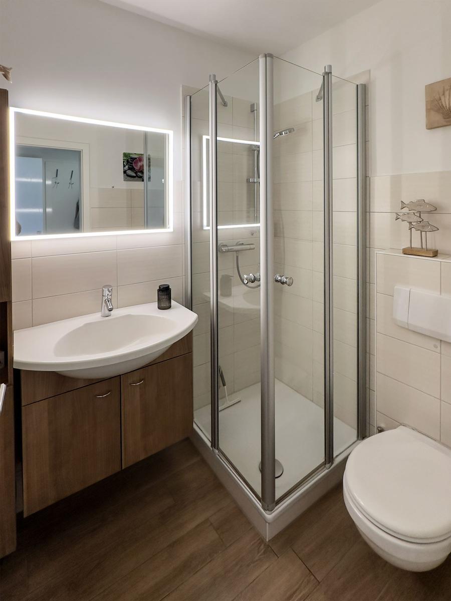 Bathroom with shower, sink and toilet. Tiled wall and wooden floor.