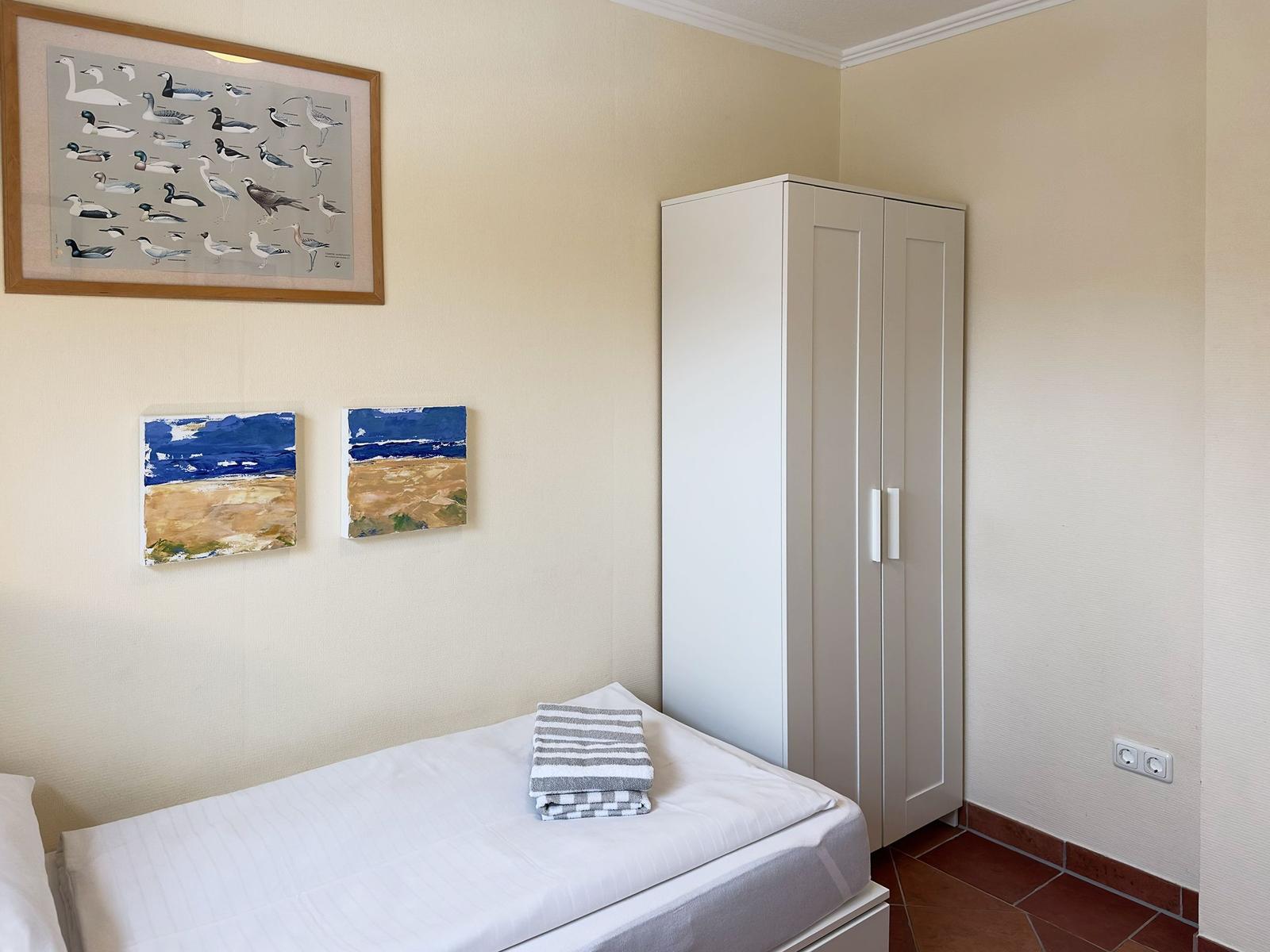 Schlafzimmer mit Bett, Kleiderschrank und Wandbildern.