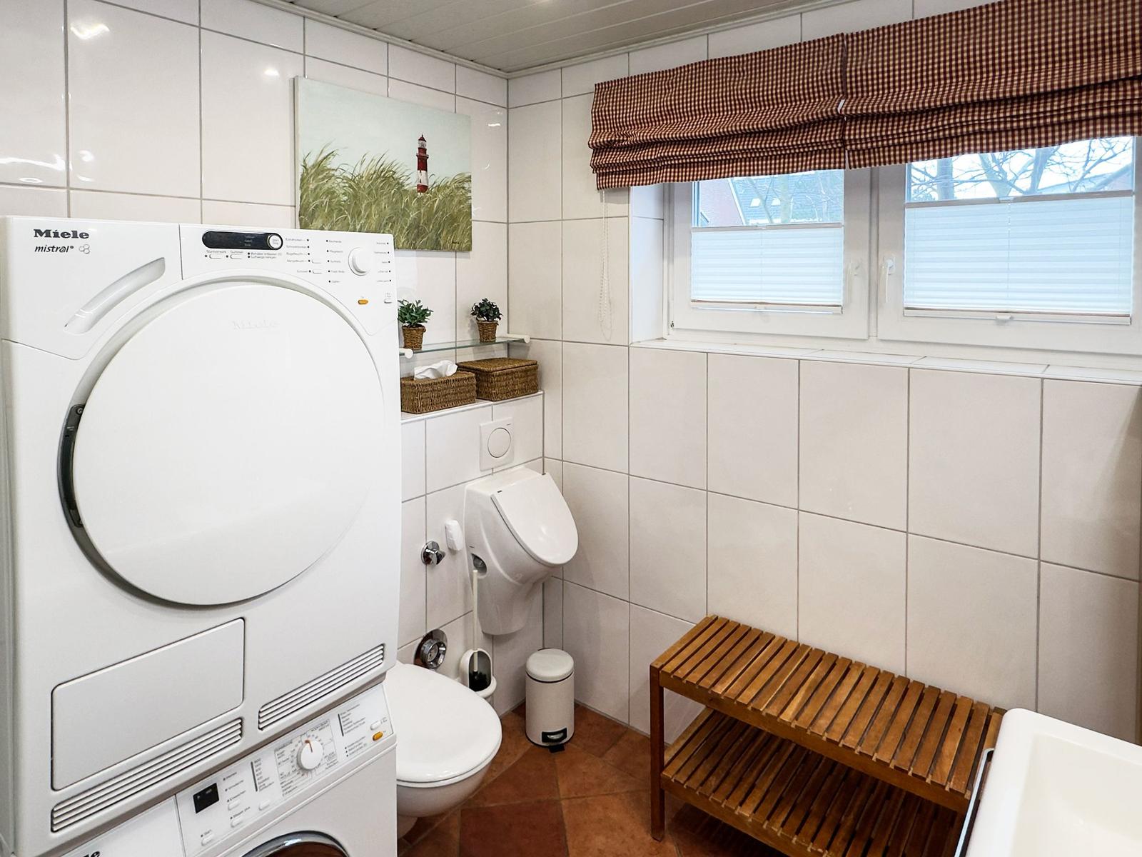 Badezimmer mit Waschmaschine, Trockner, WC und Holzbank.